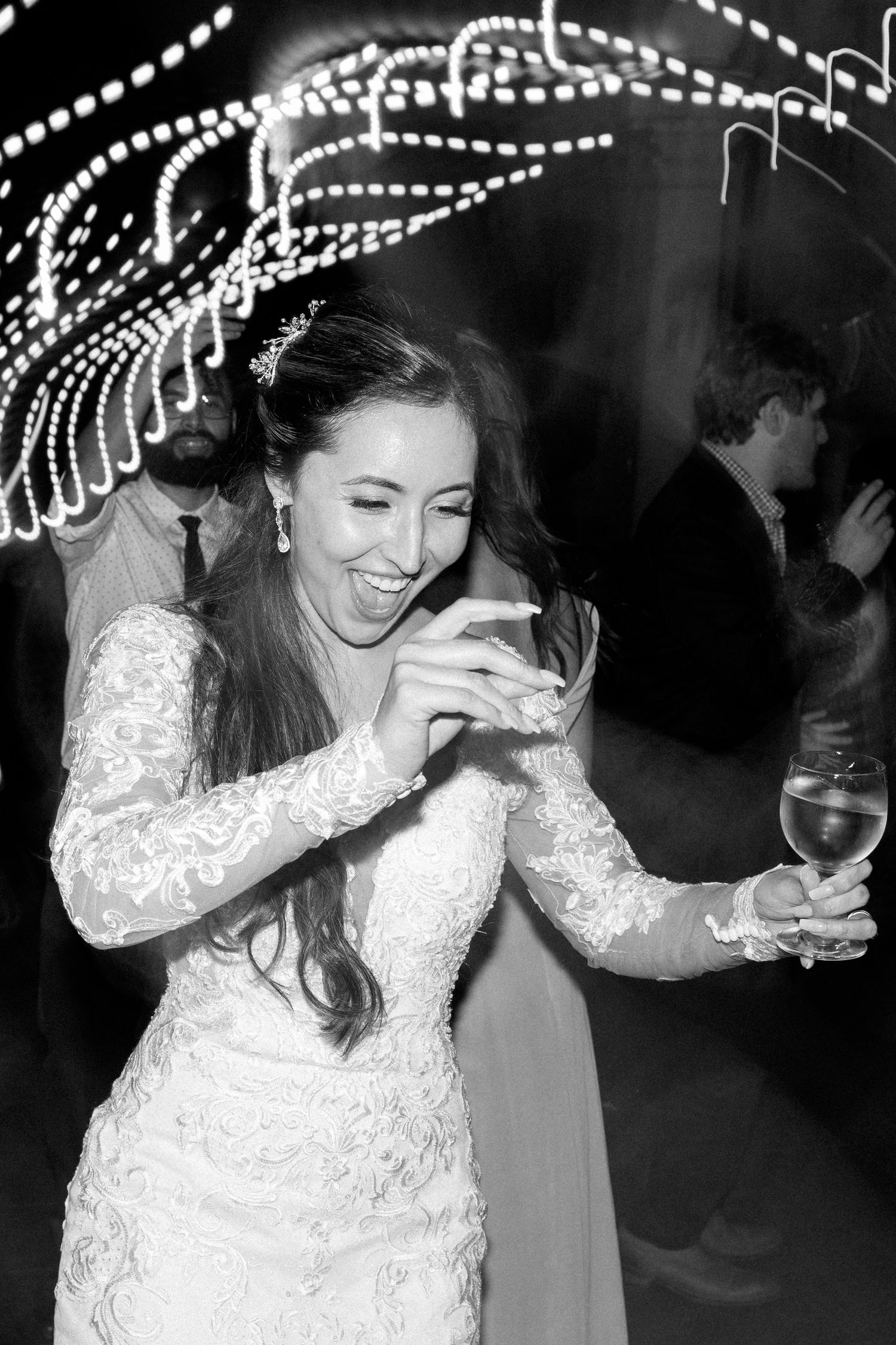 Black and white photo of bride dancing under string lights at wedding reception.