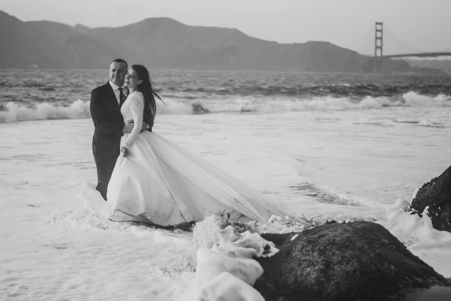A romantic black and white beach photo with the Golden Gate Bridge visible in the background.