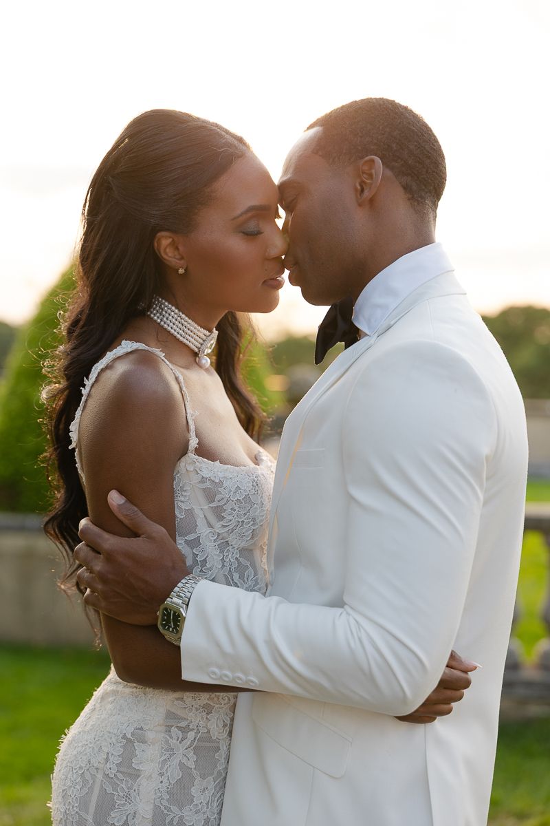 A romantic sunset wedding portrait featuring a couple in white formal attire embracing outdoors.
