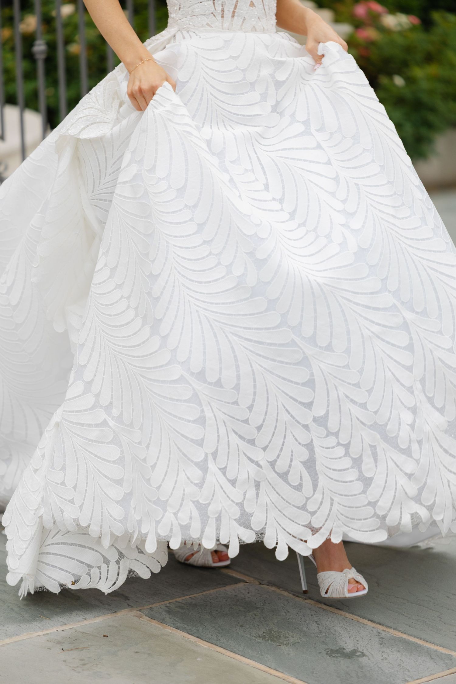 Bride wearing a stunning white ball gown with intricate leaf pattern embroidery, paired with silver heeled sandals.