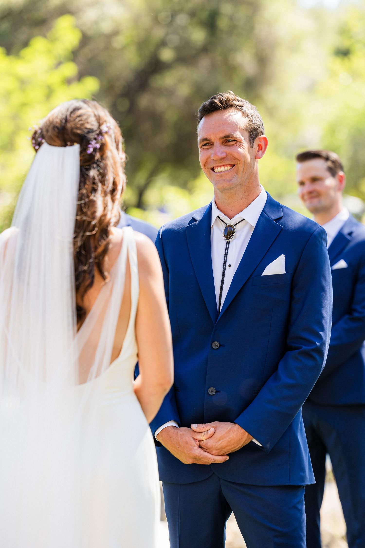 A bride and groom share a romantic moment during their outdoor wedding ceremony in navy blue attire.