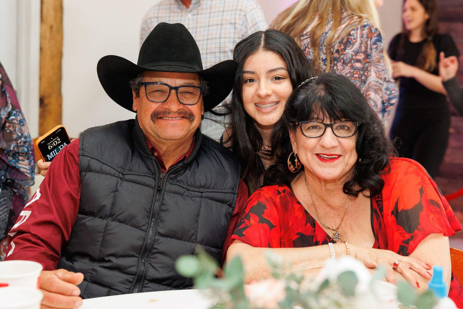 Three people smile together at a table during what appears to be a social gathering or event.