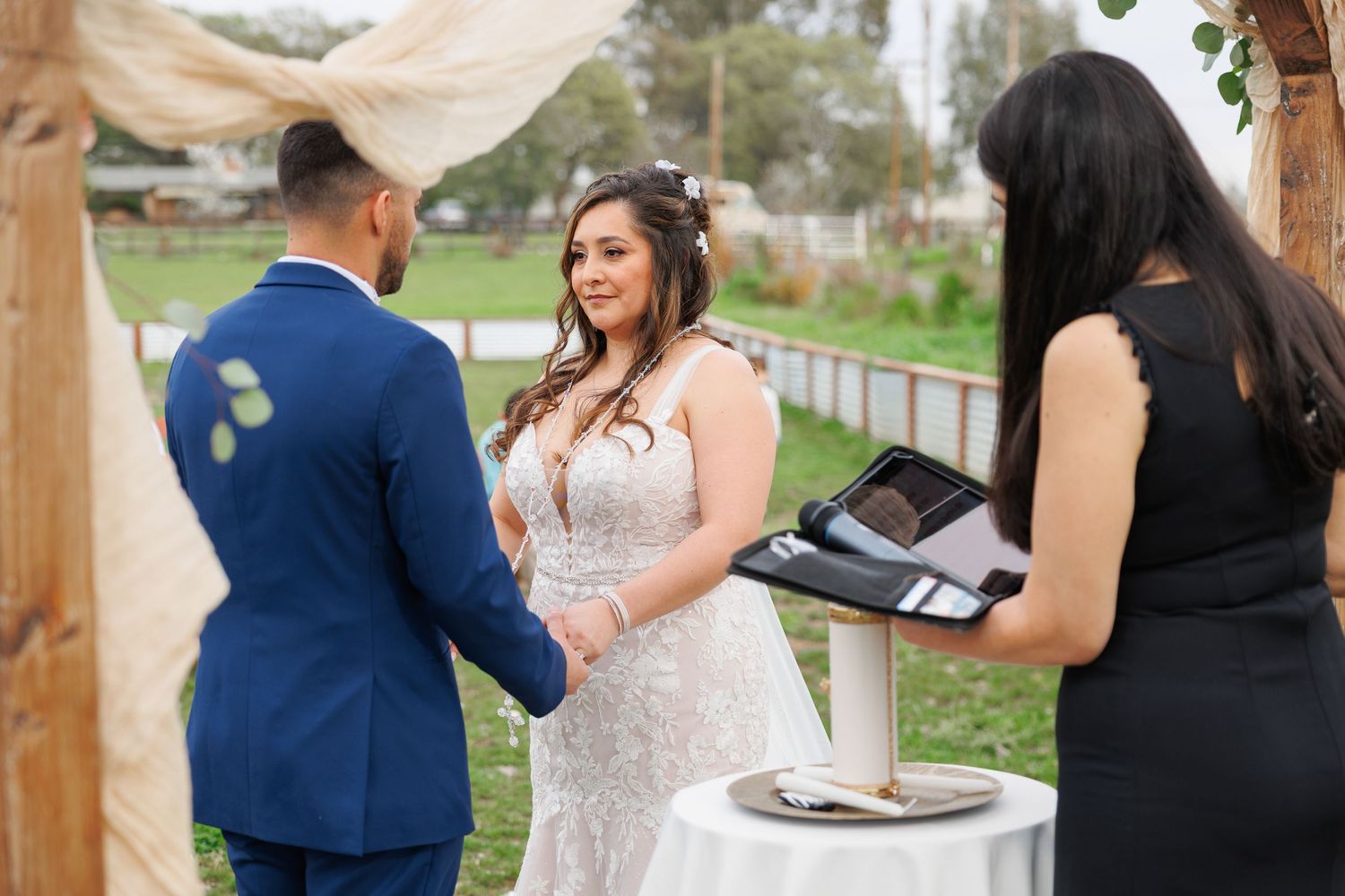 Wedding guests enjoying outdoor reception under wooden pavilion with string lights and rustic decor.
