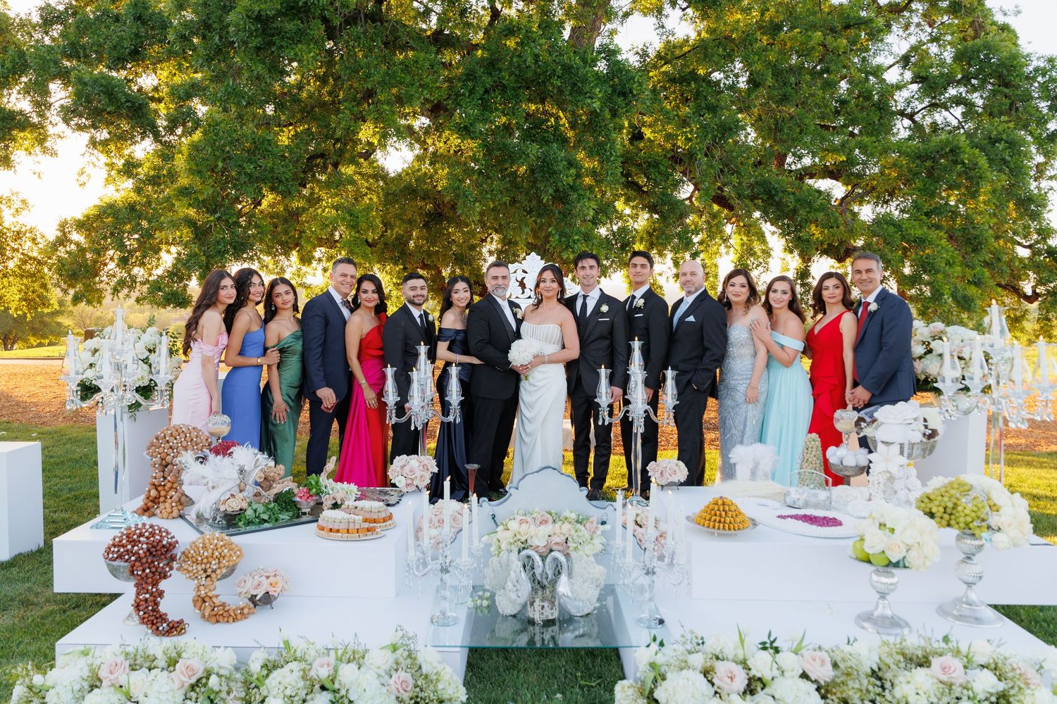 Wedding guests gather at elegant outdoor reception tables decorated with floral centerpieces and white linens at sunset.