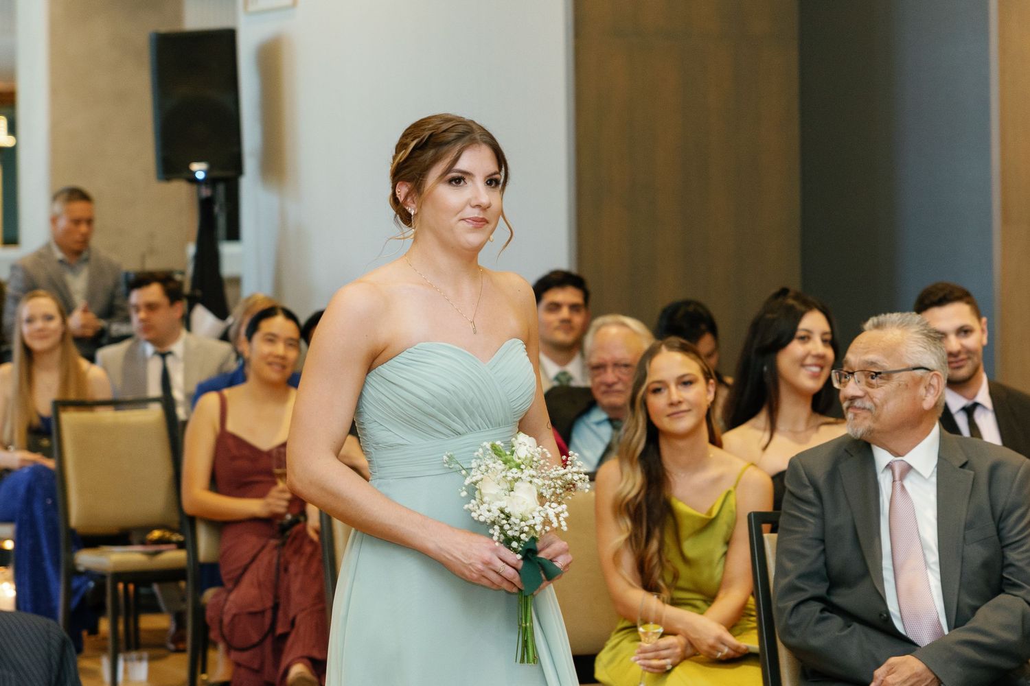 Bridesmaid in mint green strapless dress holds white bouquet while walking down aisle during wedding ceremony.