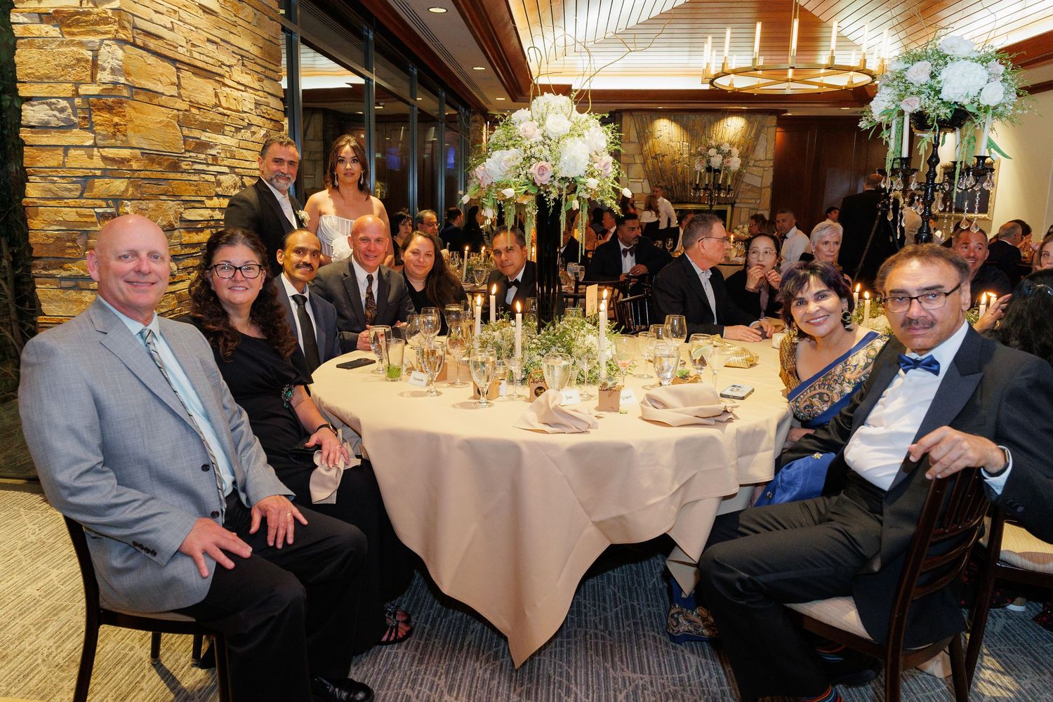 Guests seated at elegant round dining tables in a banquet hall with stone walls and warm lighting.