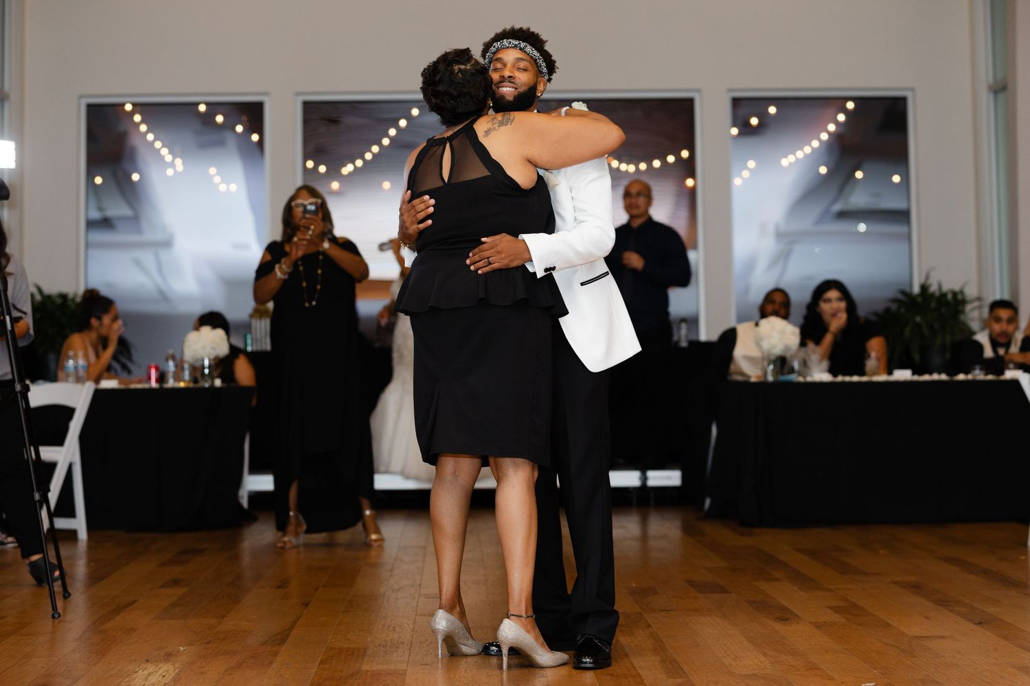Dancers move gracefully across a wooden dance floor during a formal event with string lights overhead.