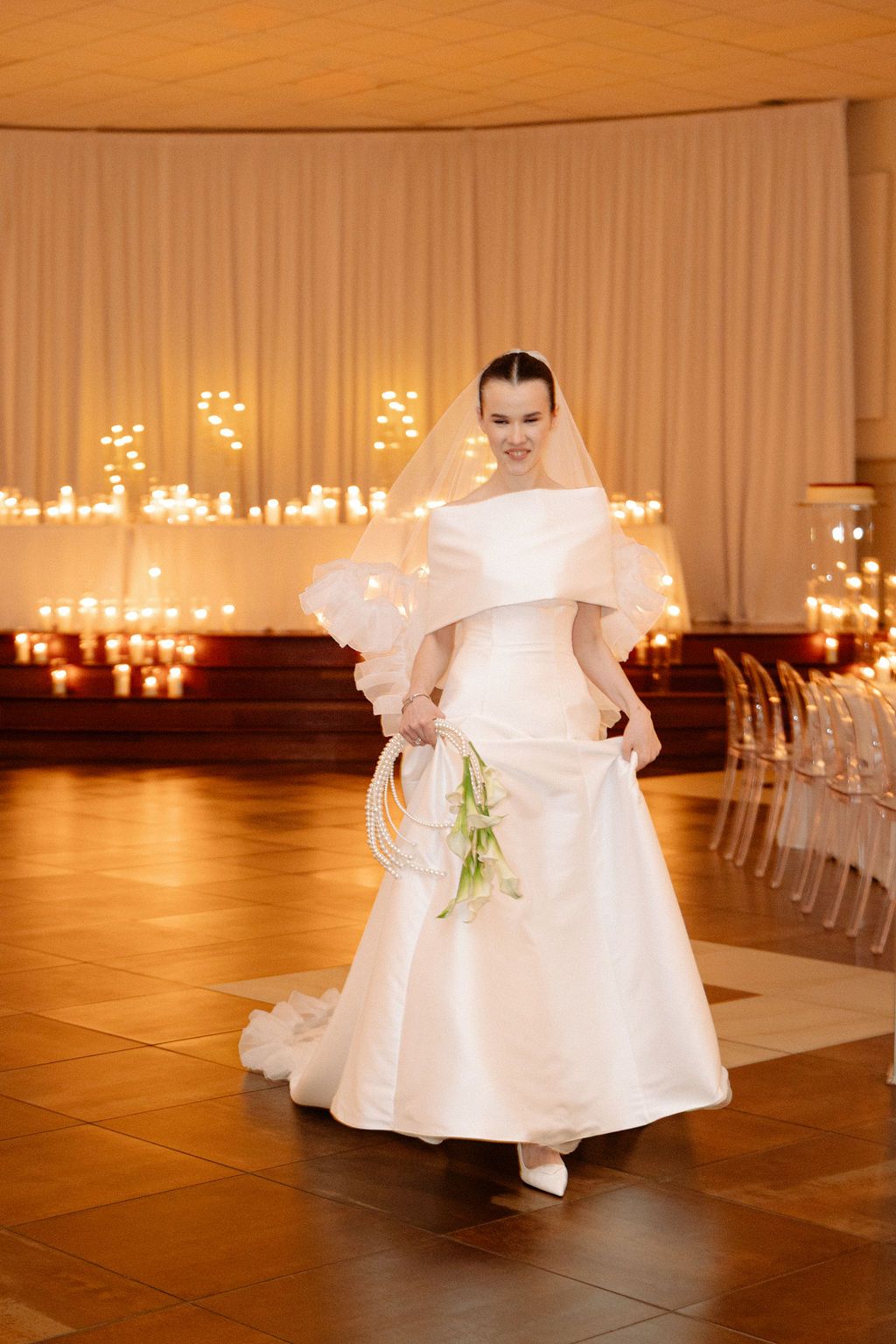 Wedding ceremony setup in warm lighting with white decor and candles along a wooden floor aisle.
