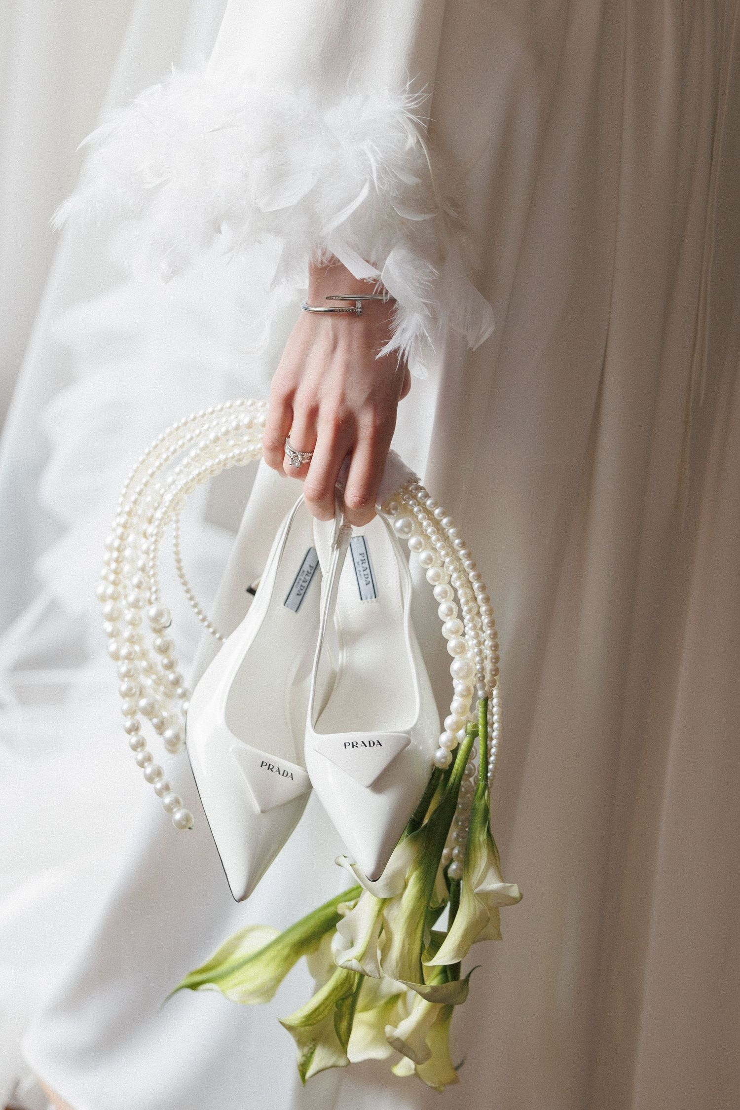A white bridal purse with pearl handles and delicate calla lily flowers arranged elegantly against a light background.