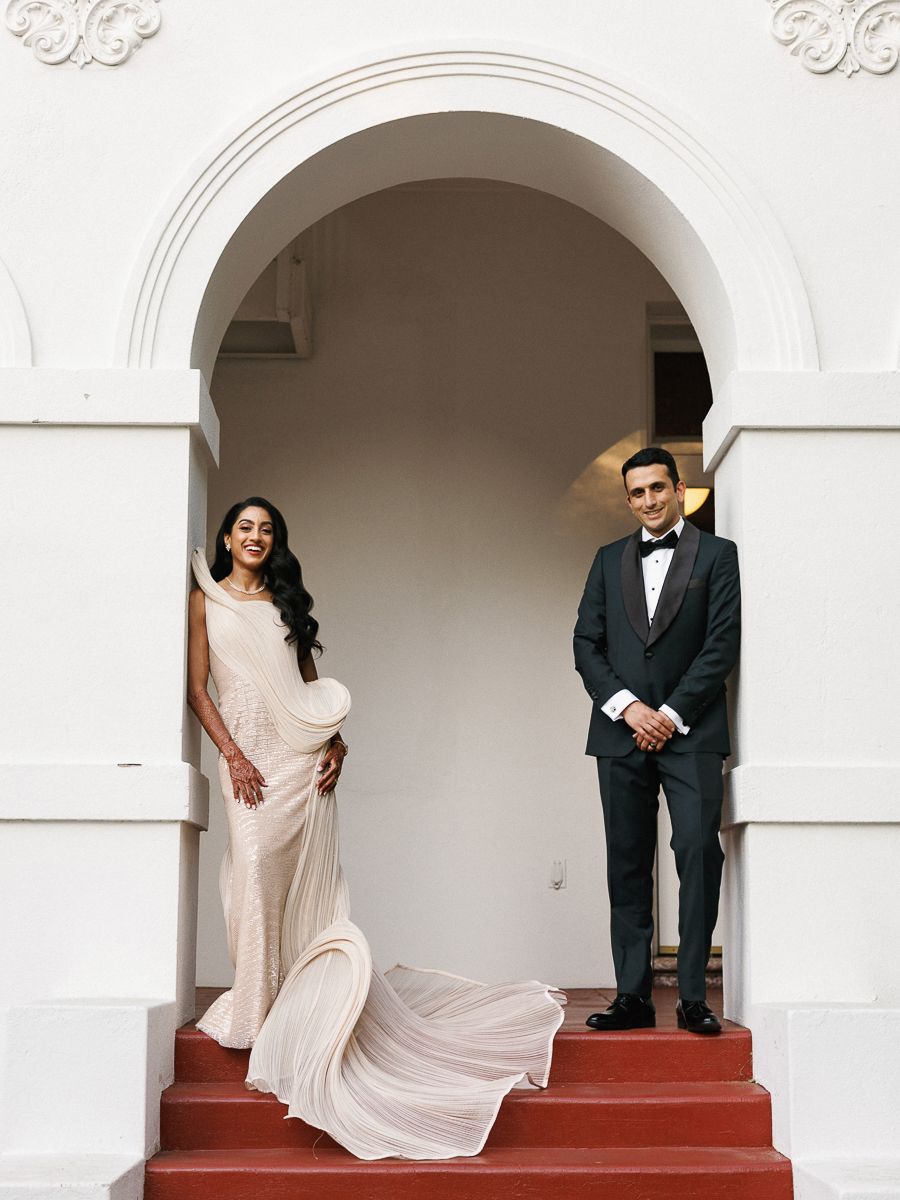 Wedding couple posing under white arched doorways in formal attire.