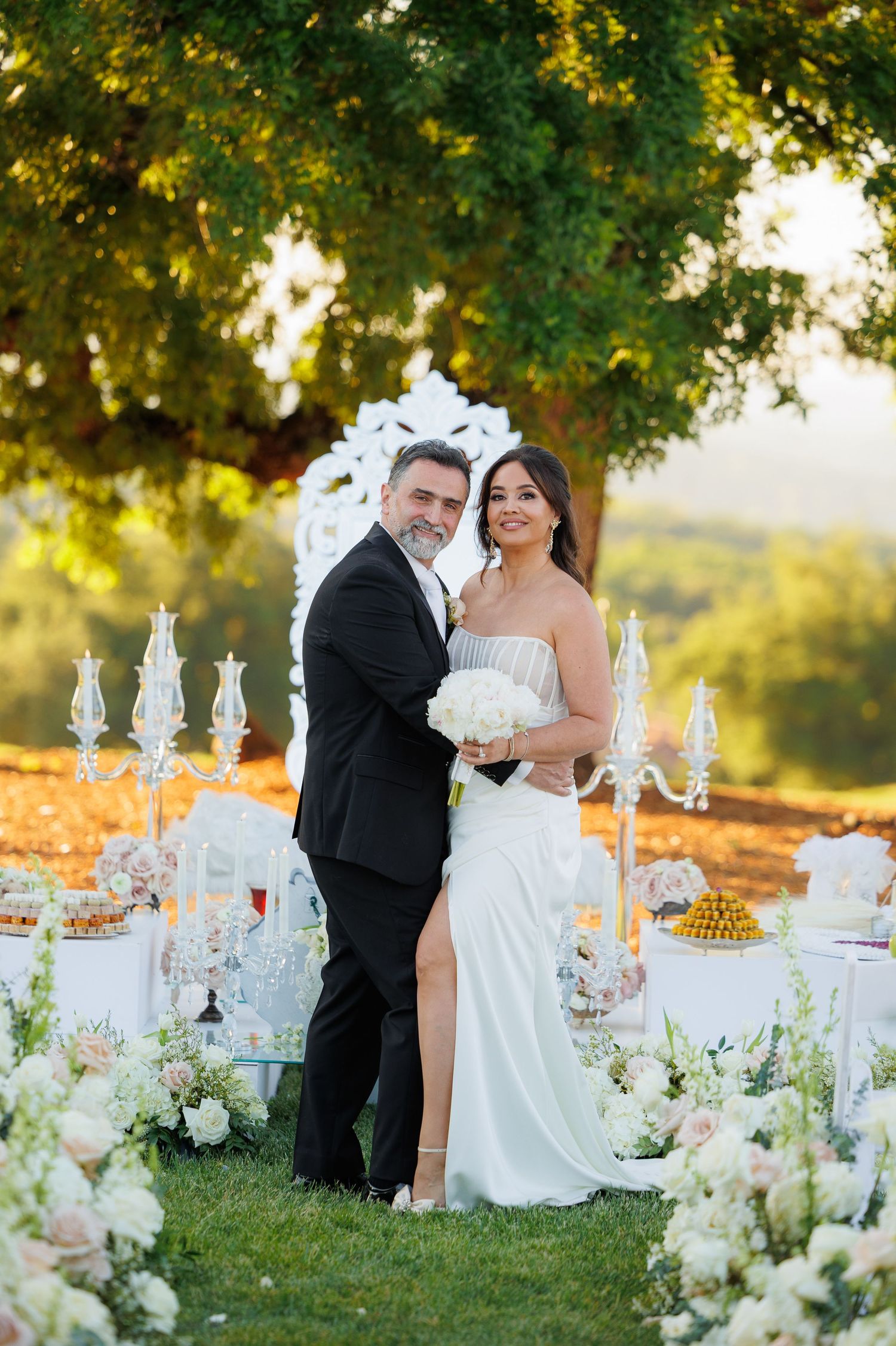Elegant outdoor wedding reception table setting with crystal candelabras and white floral arrangements at sunset.