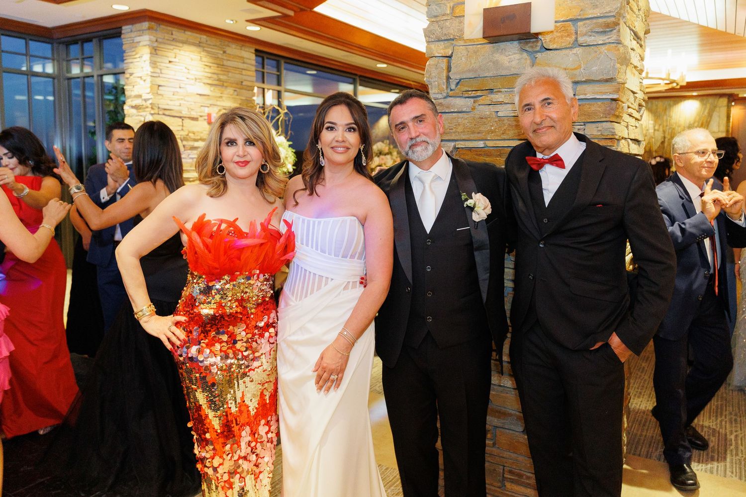 Wedding guests in formal attire dance and celebrate together on a ballroom dance floor during a reception.