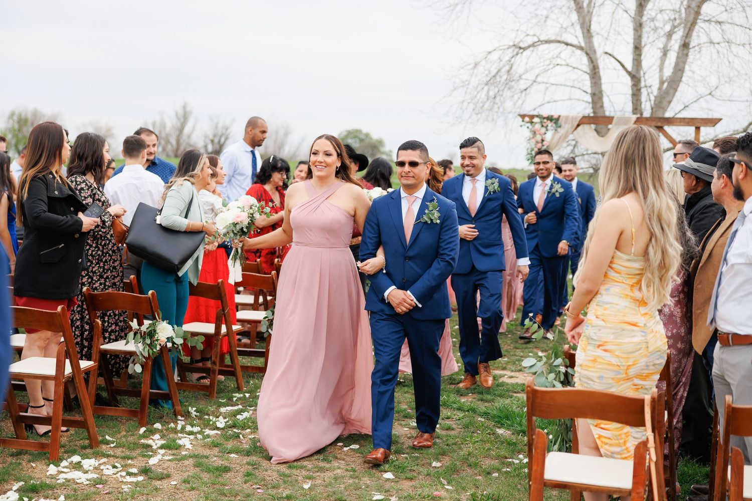 Wedding guests in blue suits and pastel dresses gather outdoors during a spring ceremony celebration.