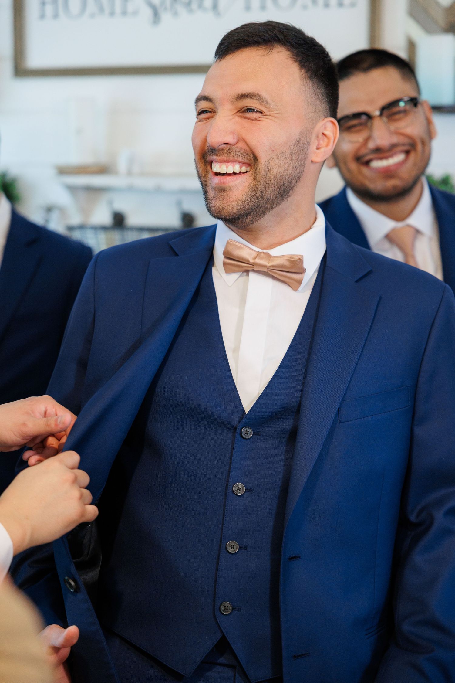 Joyful wedding guest in navy blue three-piece suit with brown bowtie laughs during celebration.