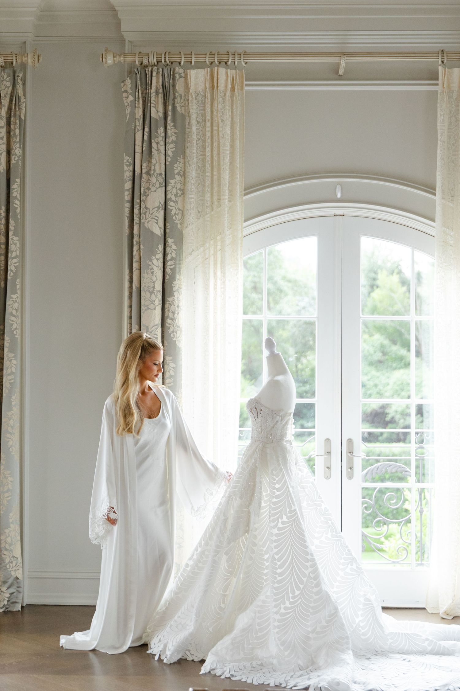 A flowing white sheer curtain billows elegantly in front of large arched windows in a bright sunlit room.