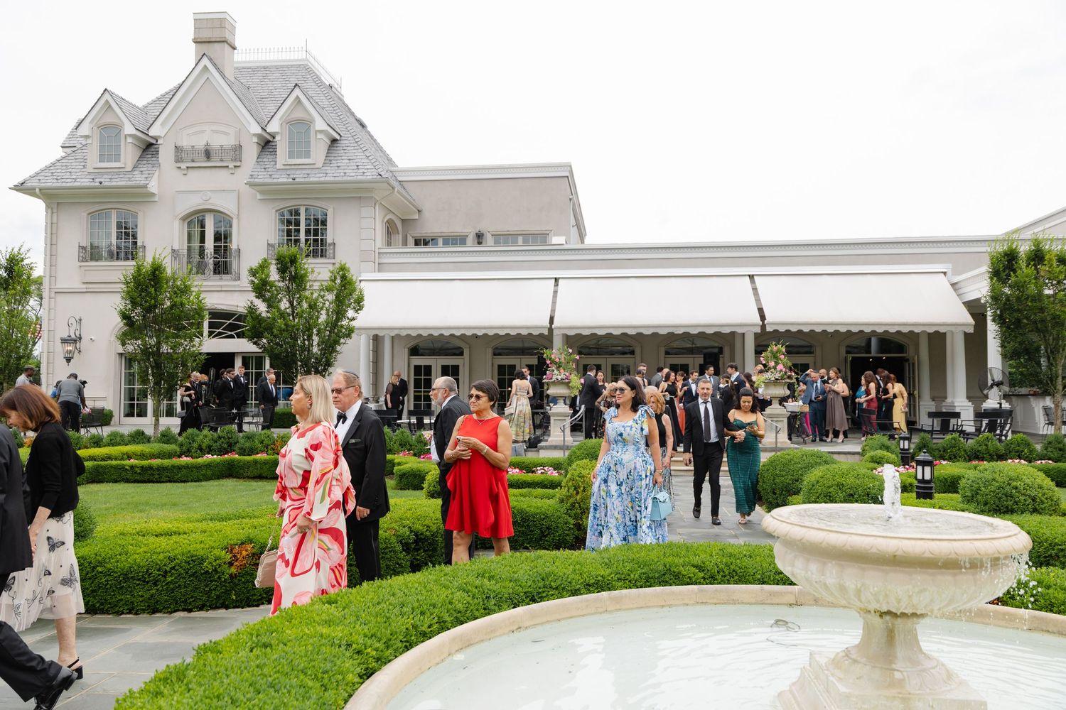 Elegant white mansion with multiple outdoor wedding reception areas and a decorative fountain in the garden.
