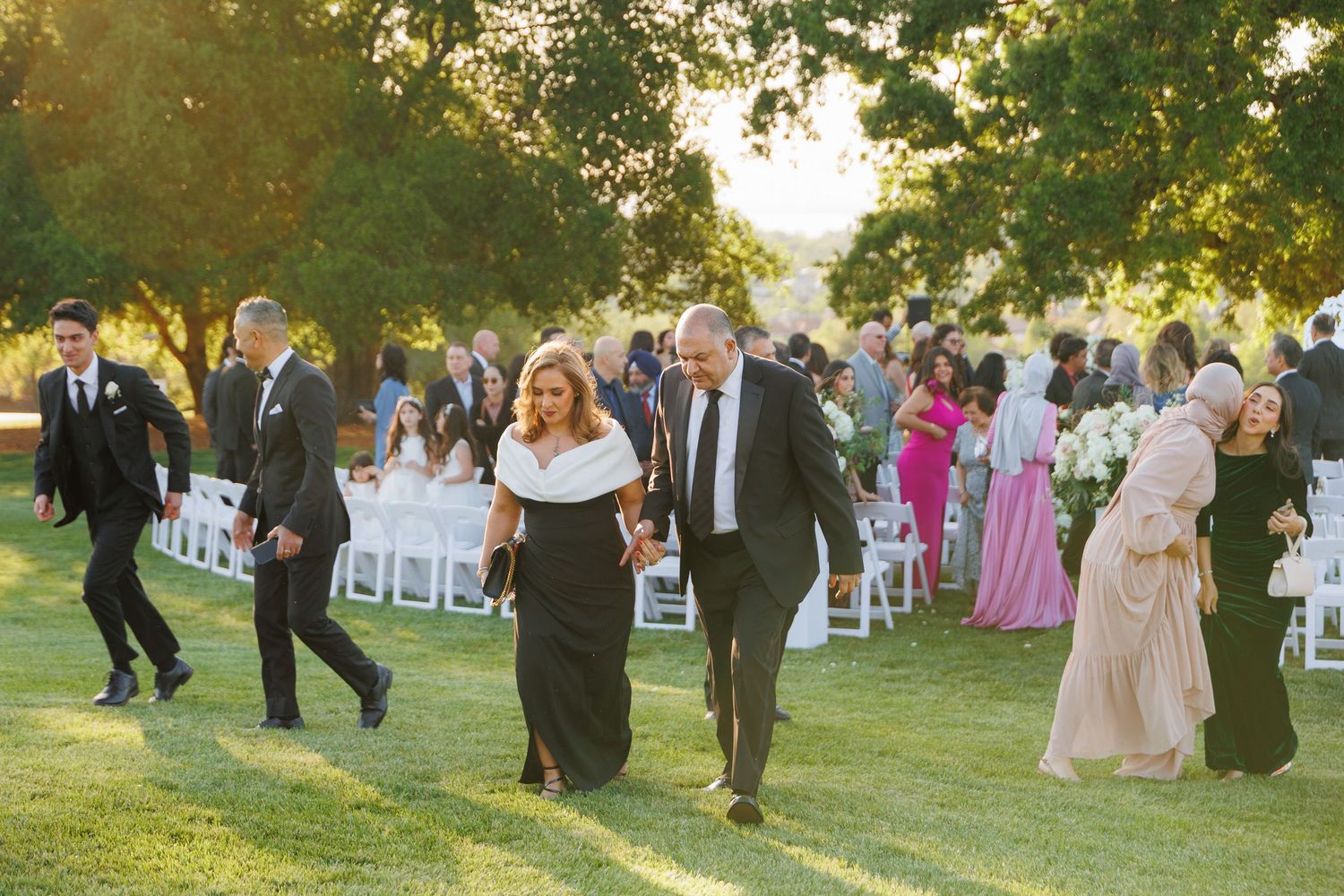 Wedding guests gather outdoors on a grassy lawn during a sunny afternoon celebration.