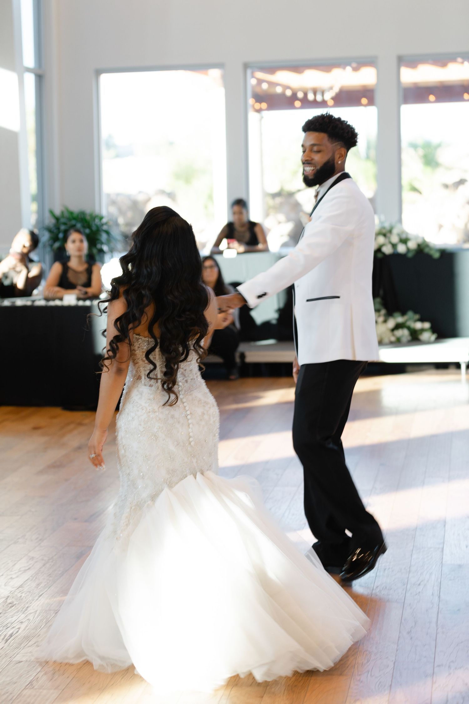 Newlyweds share their first dance on a polished wooden floor at an elegant wedding reception venue.