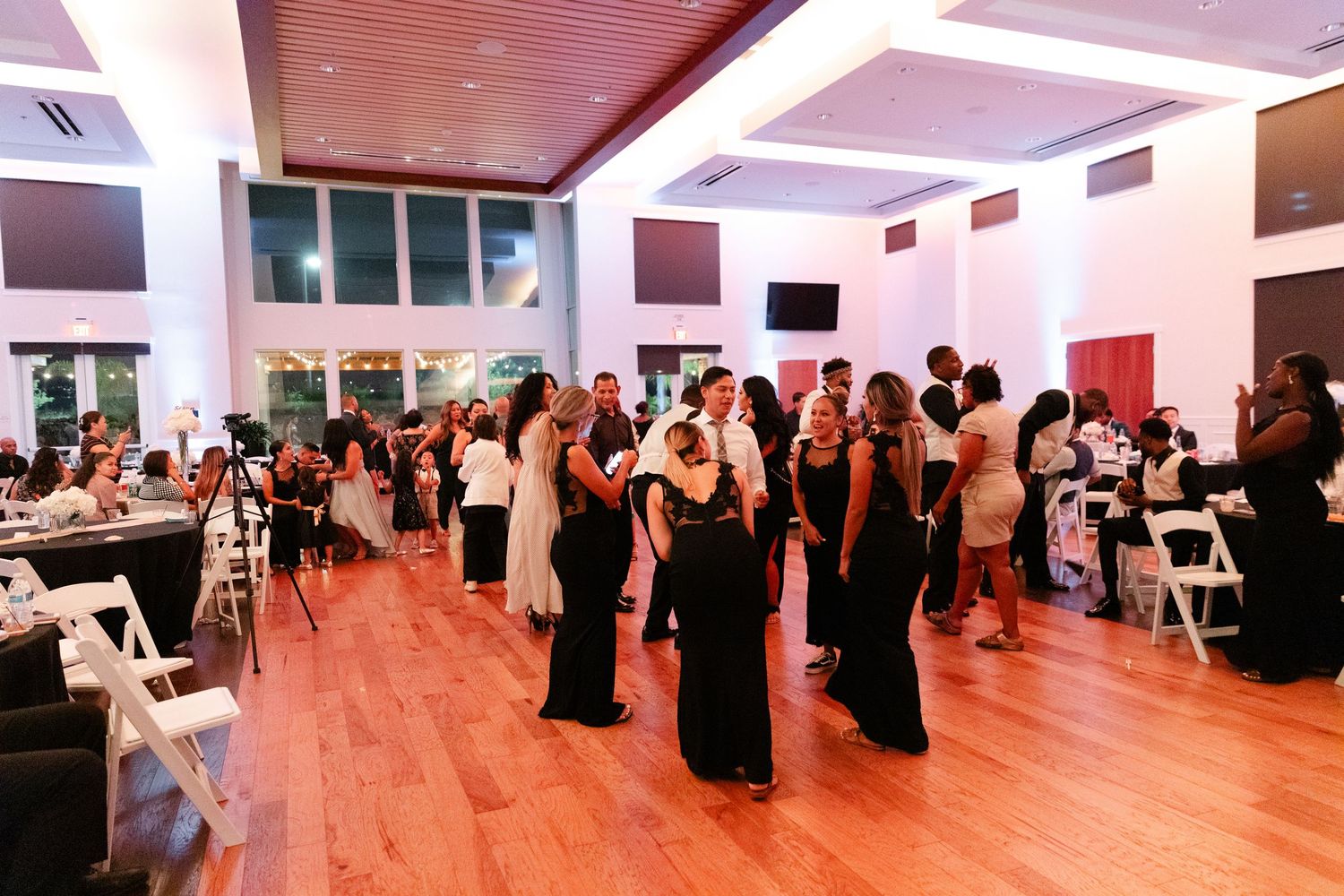 A group of people in black attire perform synchronized movements during a dance class in a bright studio space.