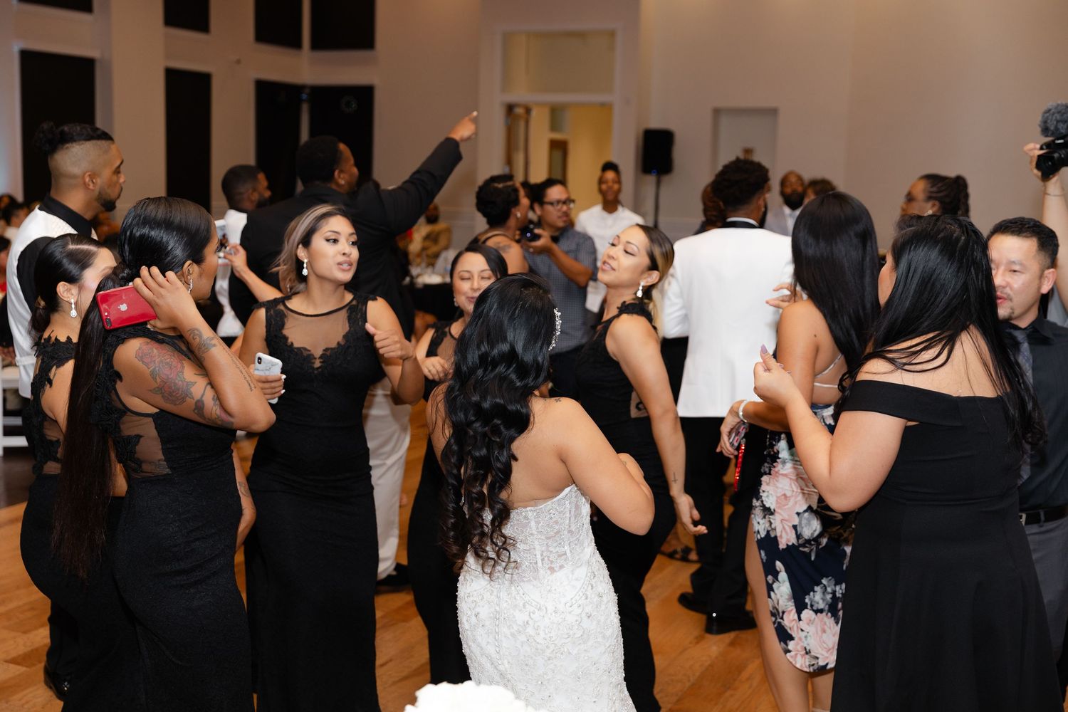 Wedding guests dance and celebrate together on a crowded dance floor at an indoor reception venue.