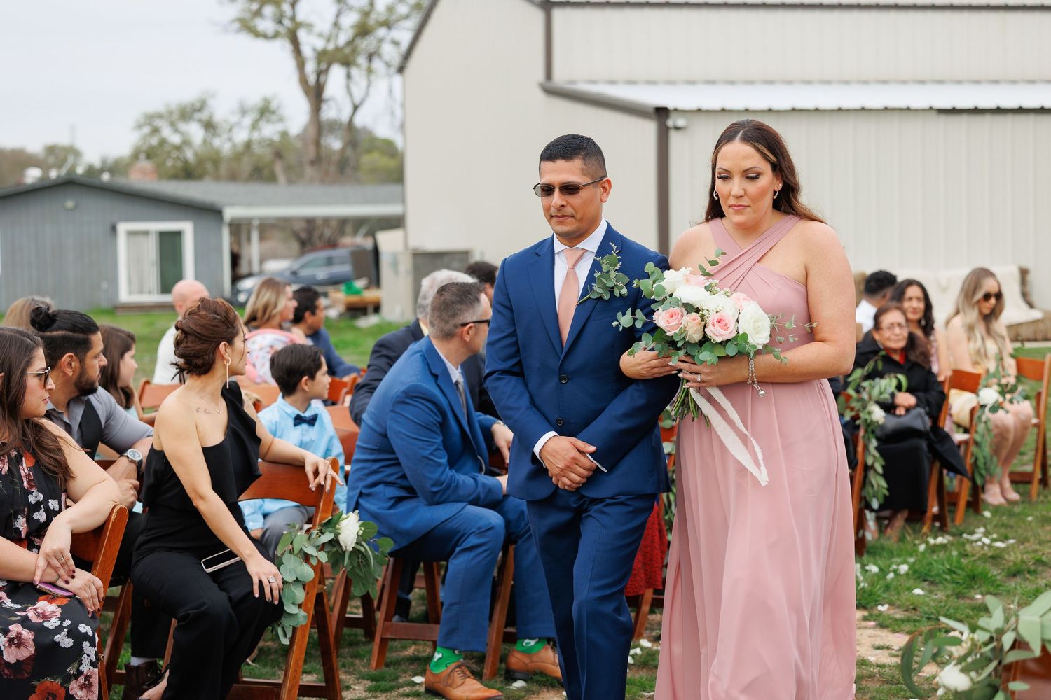 Wedding party in pink and navy blue attire pose together outdoors during a rustic countryside celebration.