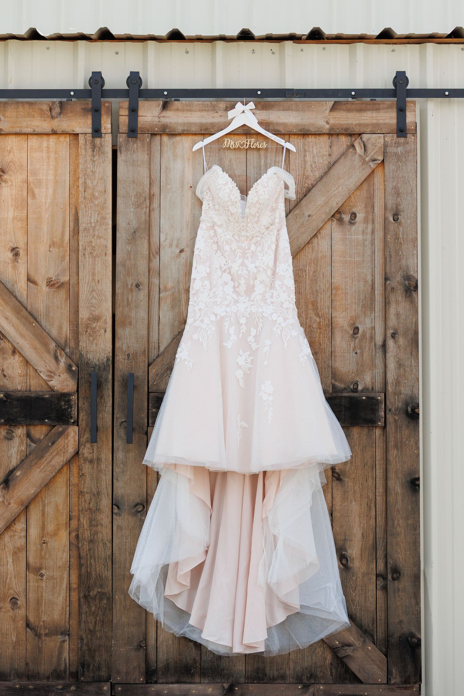 Elegant white lace wedding dress with sweetheart neckline displayed on wooden barn door backdrop.