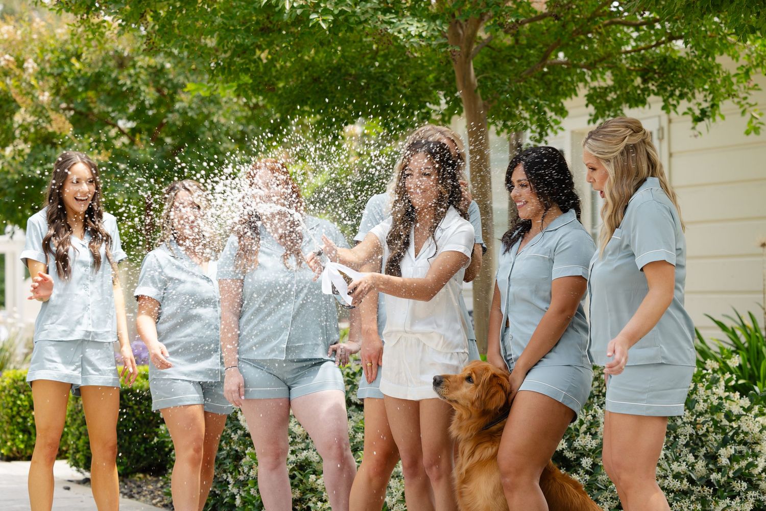 Group of women in matching white shirts and denim shorts posing together outdoors.