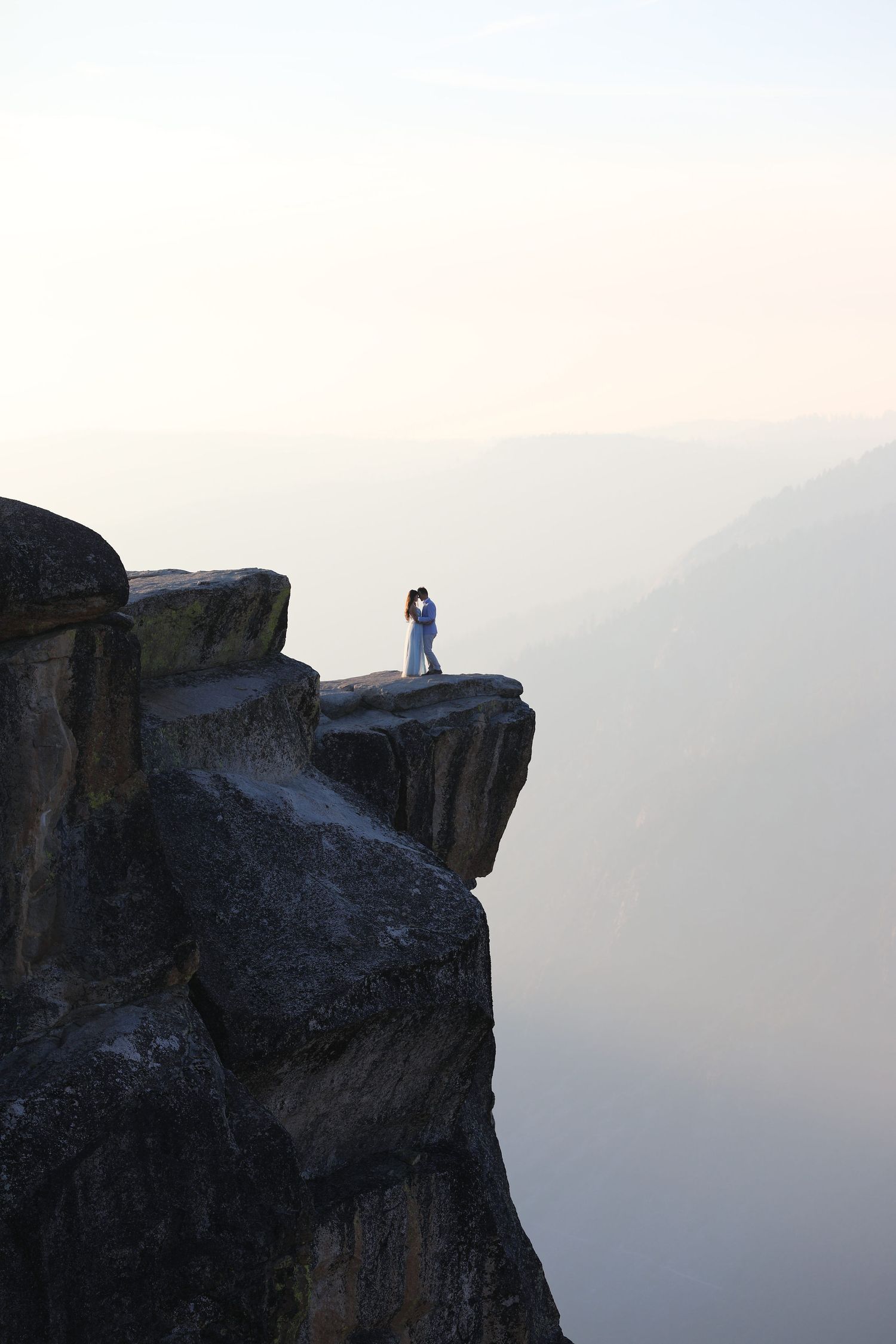 Dramatic silhouette of figures standing on cliff edge against misty mountain backdrop.