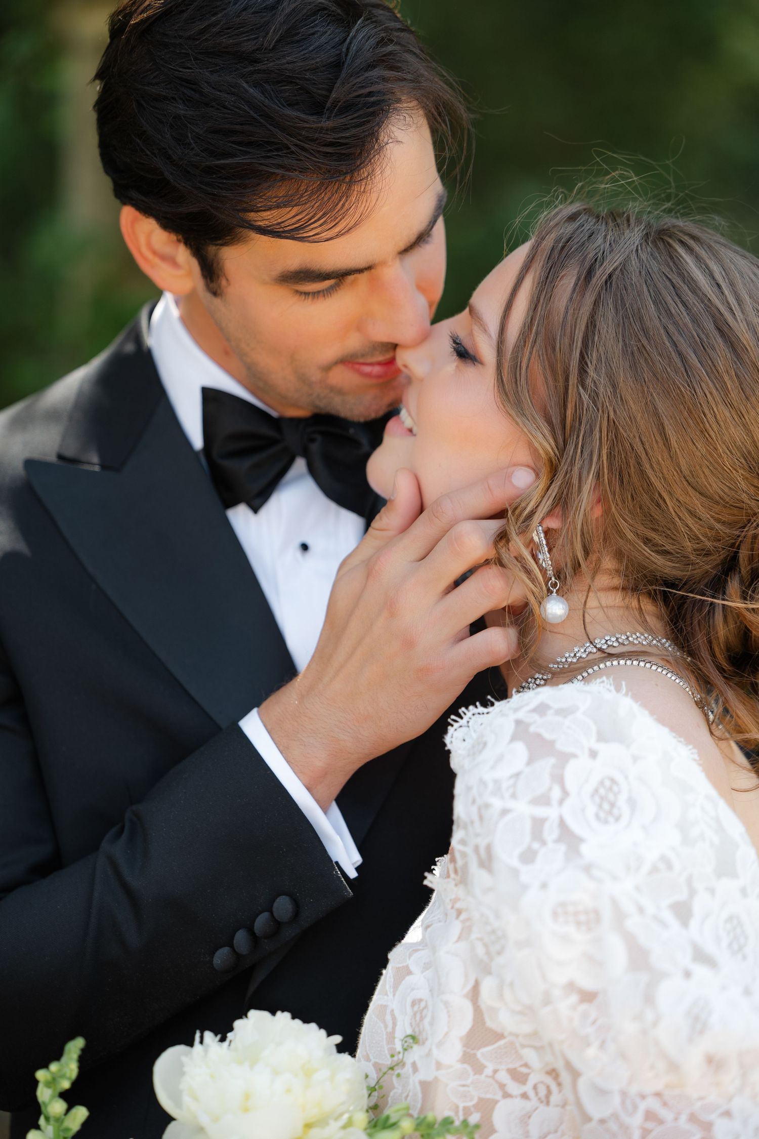 A romantic wedding couple shares intimate moments in a garden setting wearing traditional formal attire.
