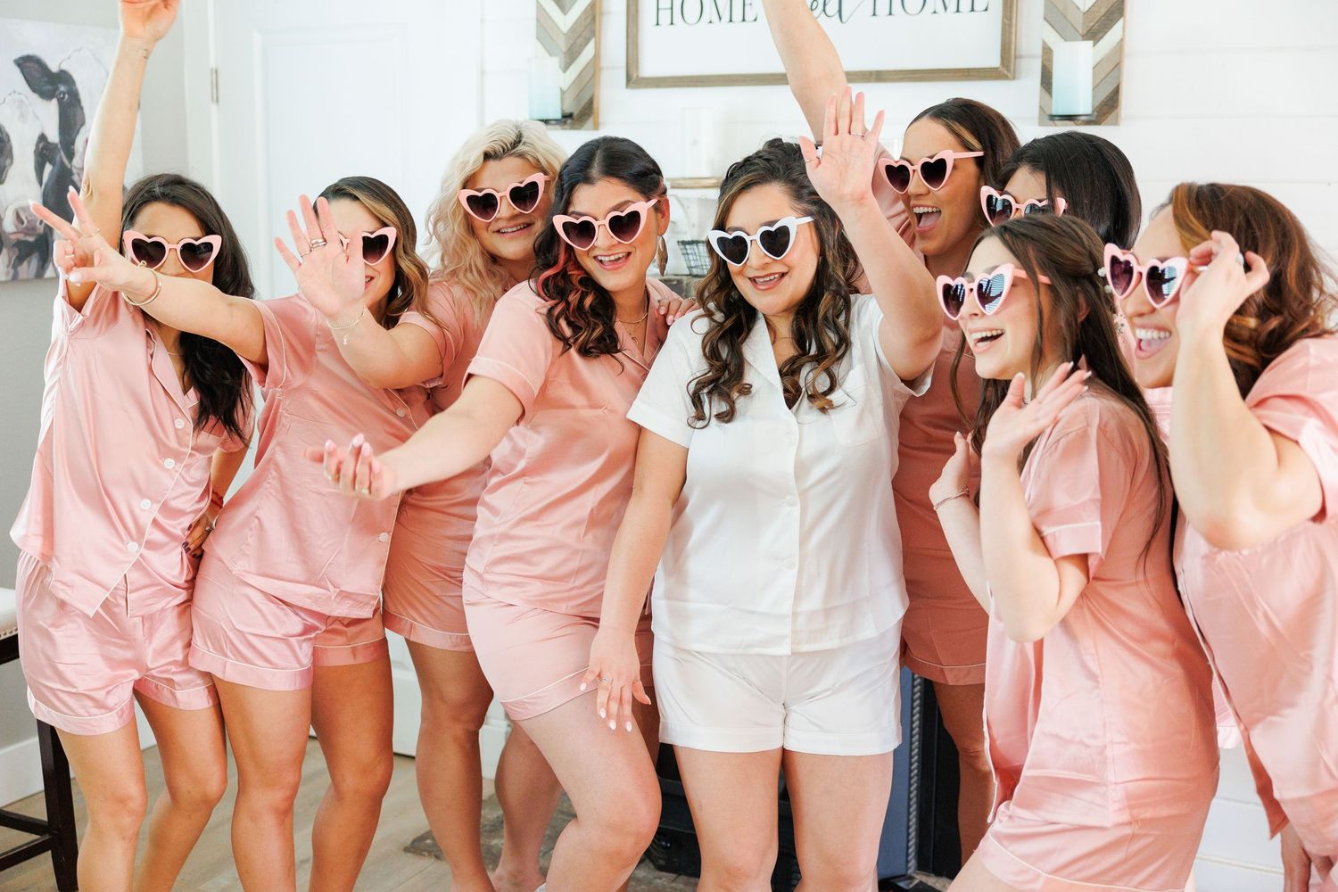 Wedding party wearing matching pink robes and sunglasses pose playfully together for photos.