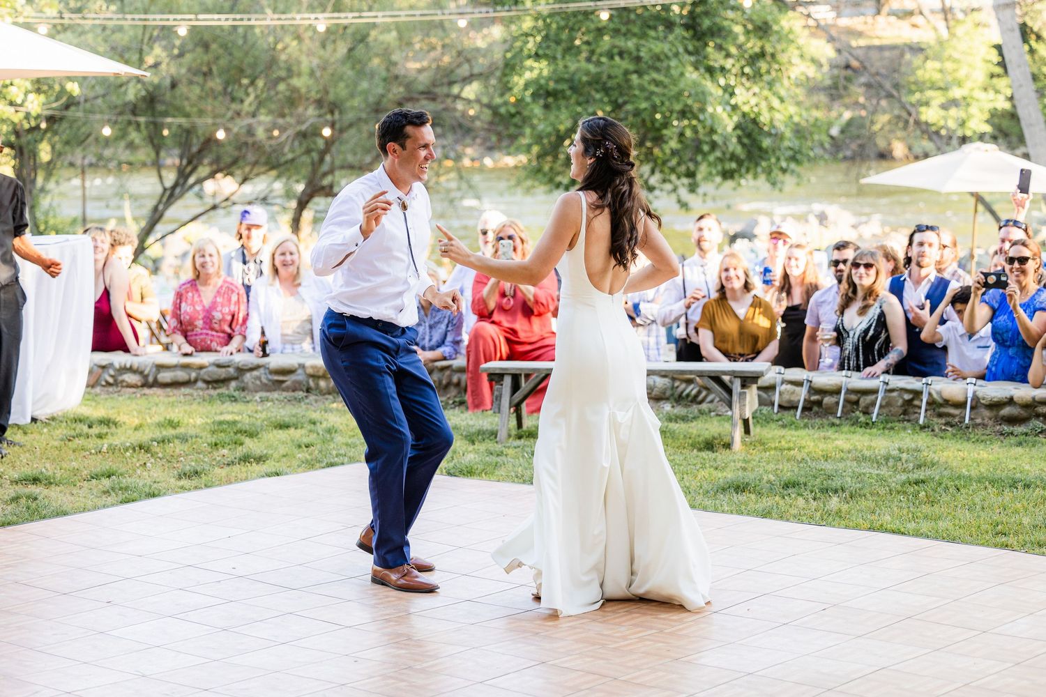 Couple dancing outdoors at a wedding celebration with guests watching in the background on a sunny day.