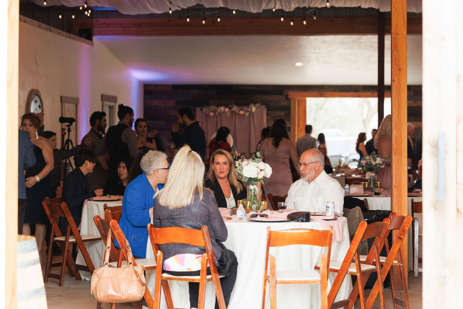 Guests seated at wooden tables during an indoor event with white walls and hanging lights.