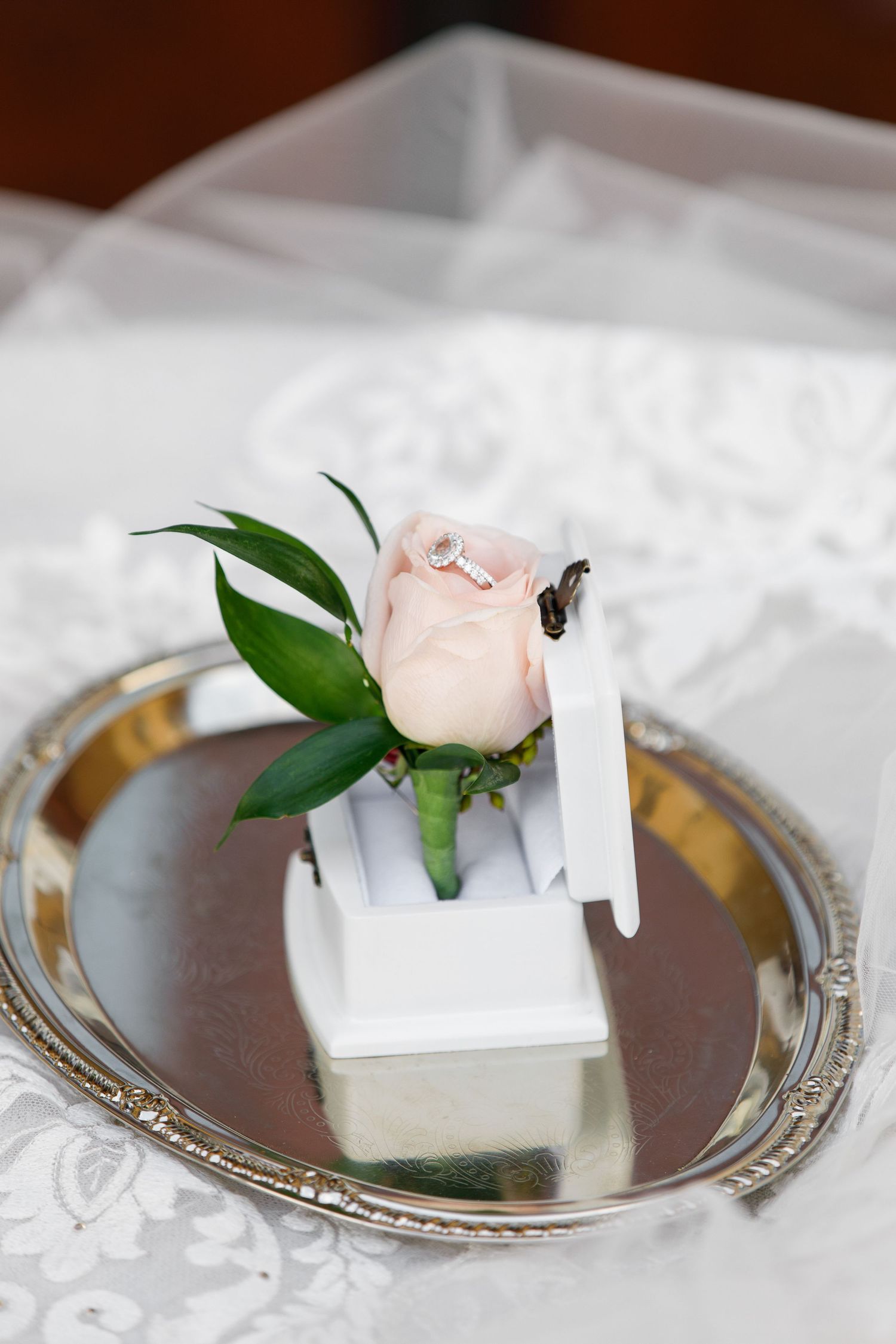 Elegant place card holder with a delicate pink rose and green leaves on a silver-rimmed plate.
