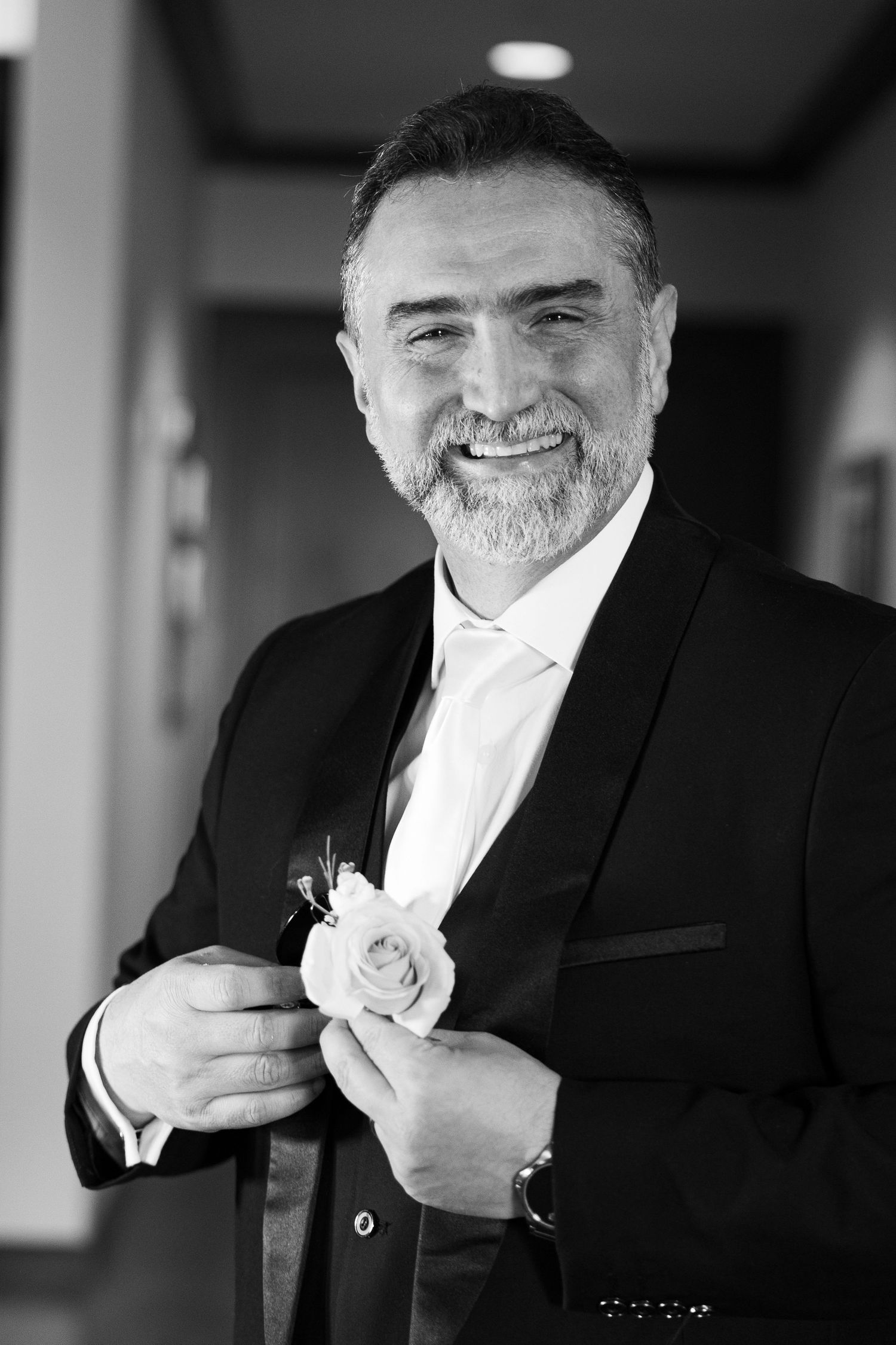 Black and white photo sequence showing someone in a suit adjusting their tie and boutonniere while smiling warmly.