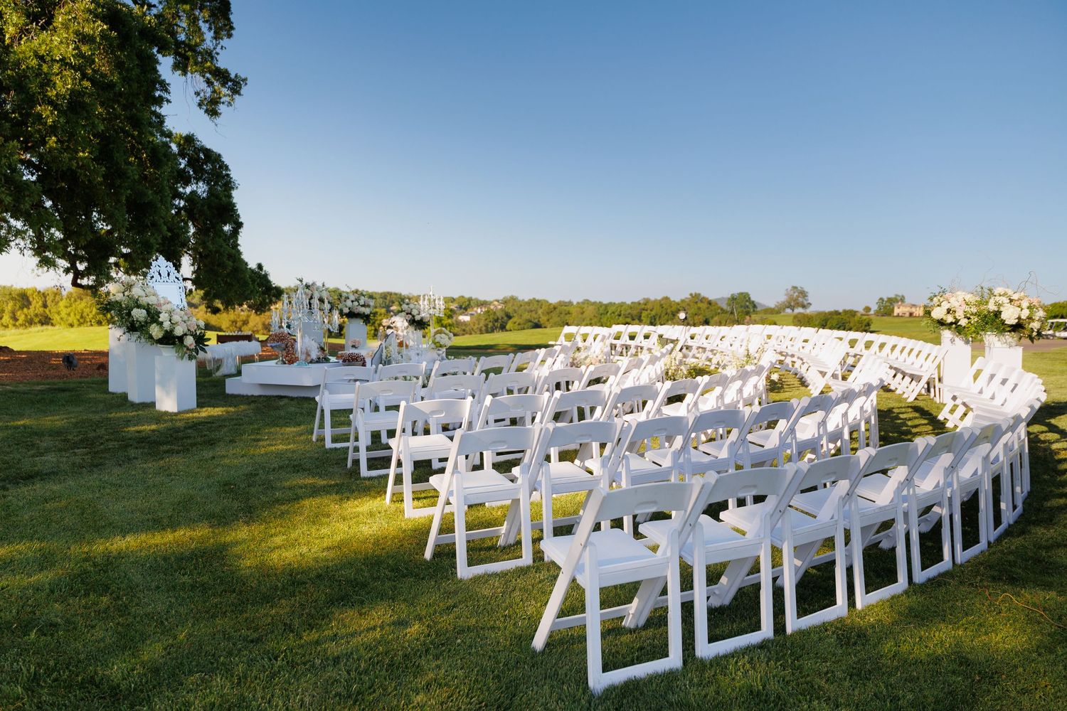 White folding chairs arranged in rows on a grassy hillside for an outdoor wedding ceremony.