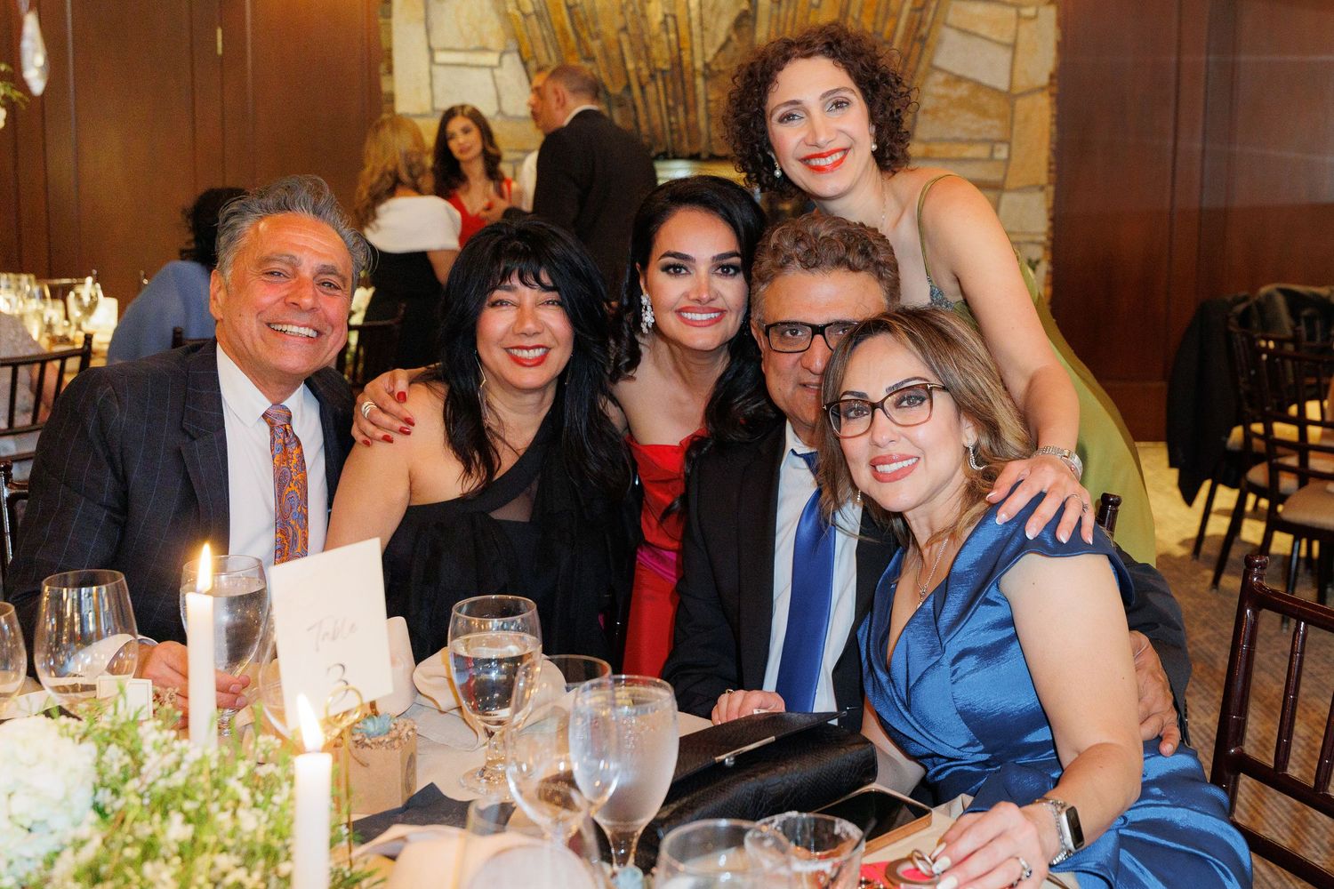 A group of people enjoying dinner and drinks together at a formal gathering with multiple tables.
