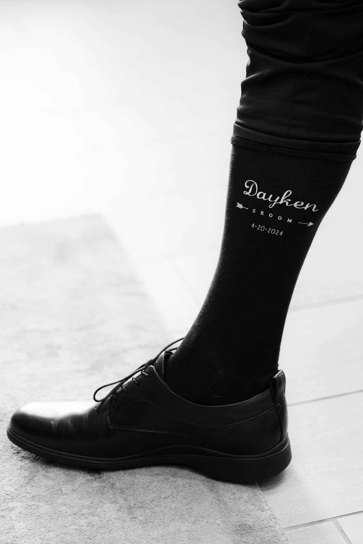 Close-up view of black leather dress shoes and dark socks on a light-colored floor.