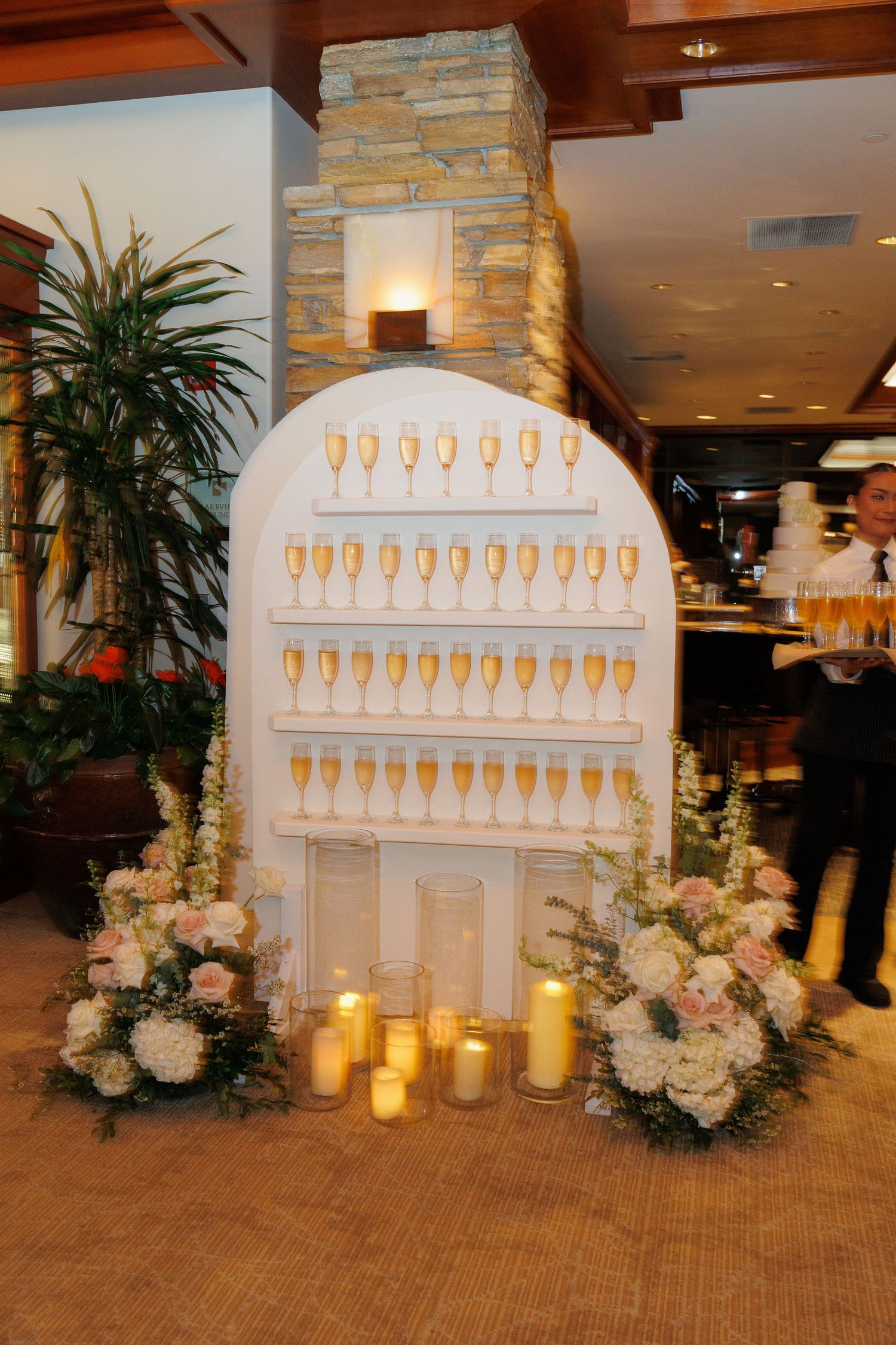 Elegant wedding seating chart display with illuminated champagne glass design and floral arrangements on wooden floor.