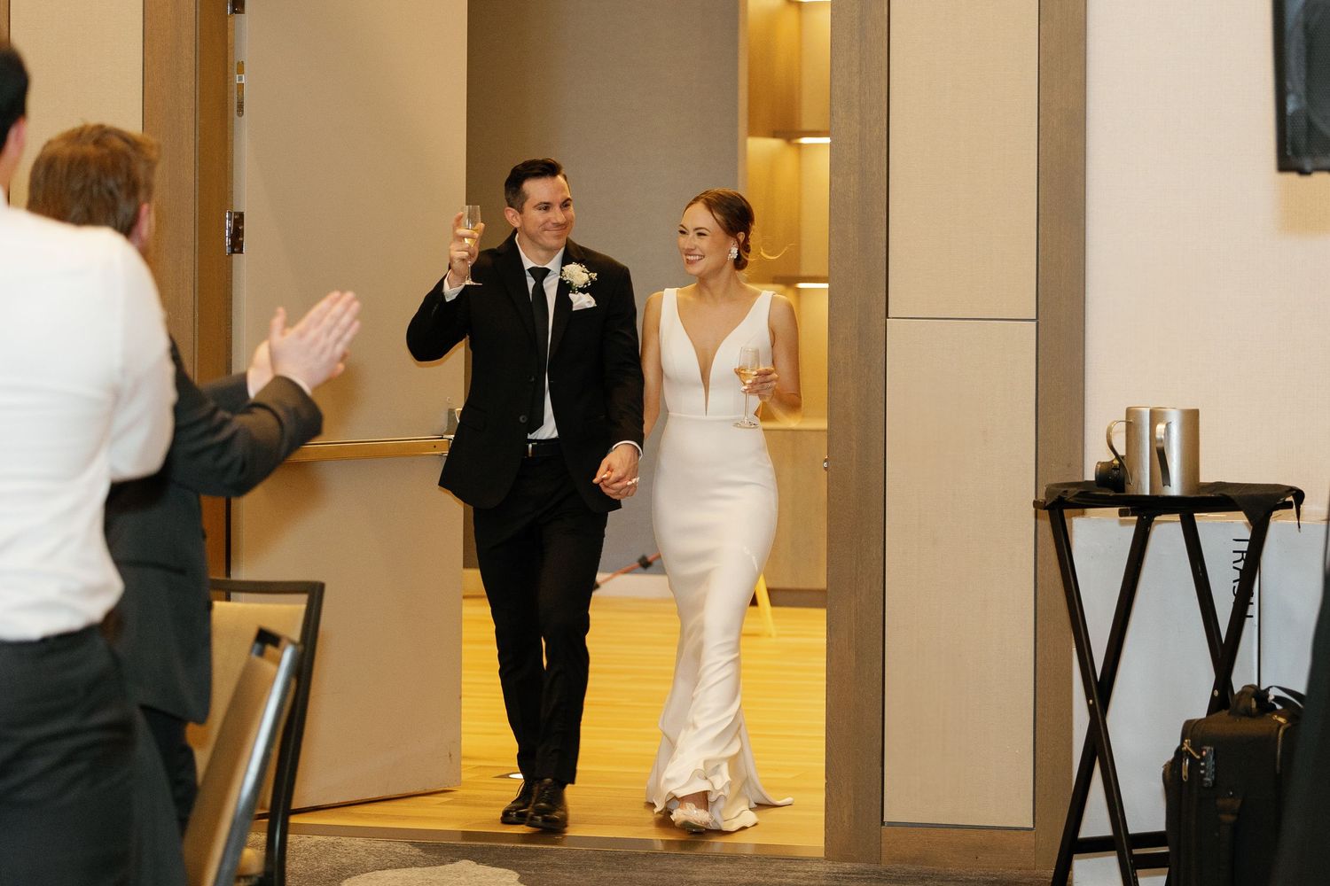 Wedding party members in formal attire interact in a warmly lit indoor venue hallway.