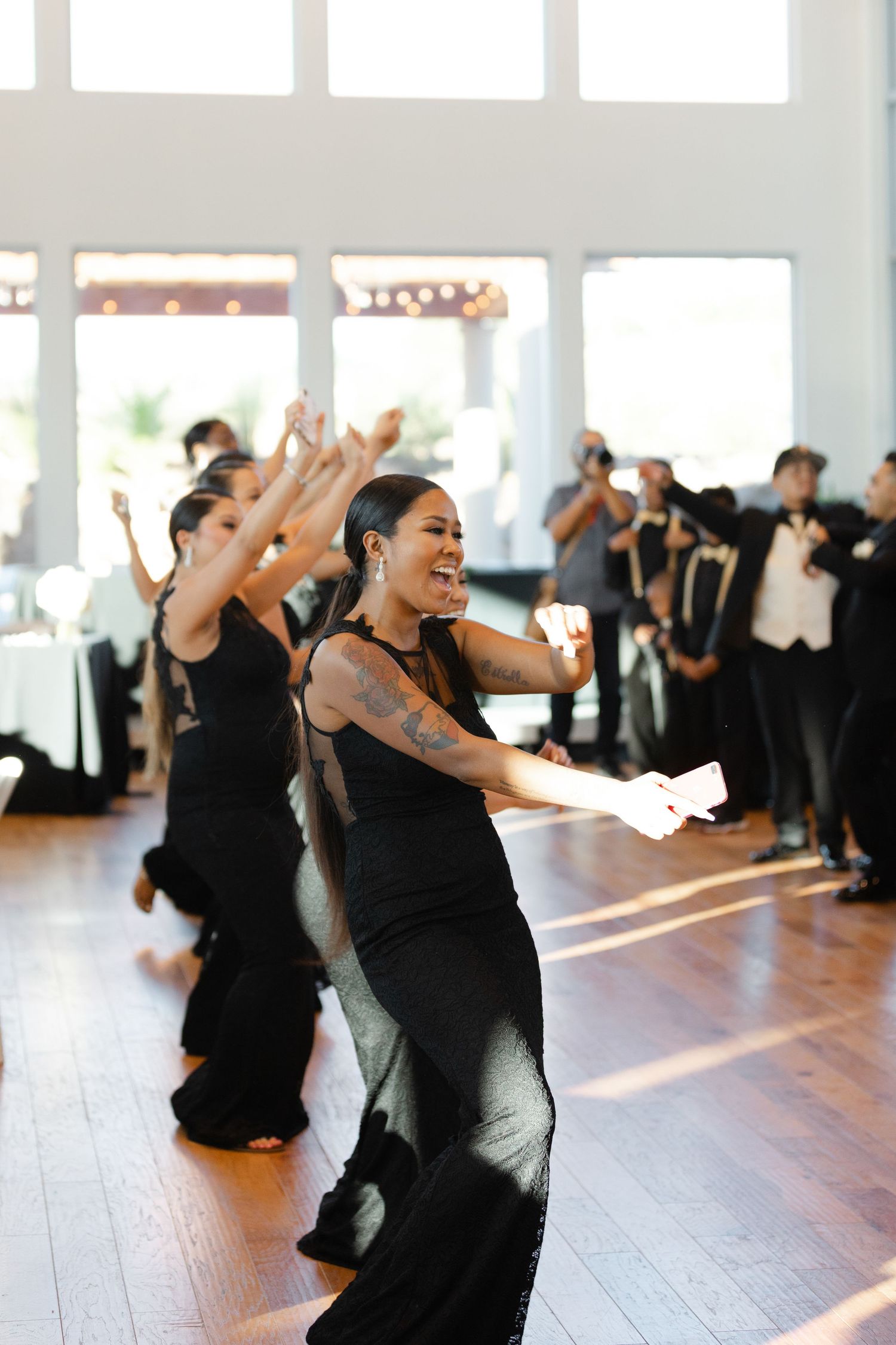 Dance class participants in black attire practice energetic movements together in a bright studio space.