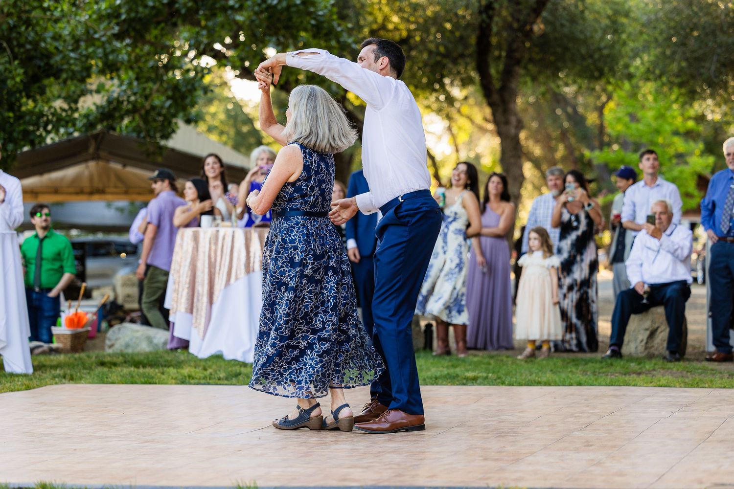 Wedding guests dance and celebrate together outdoors at a garden reception during golden hour.