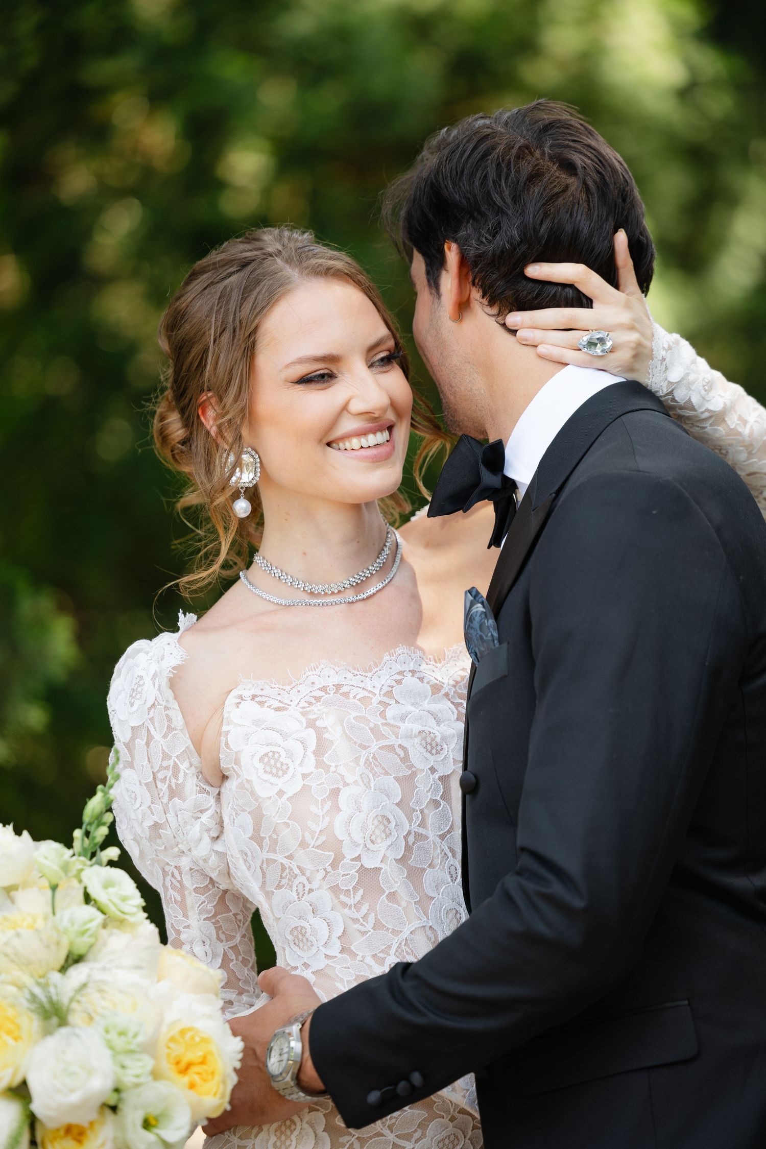 Romantic wedding couple in white lace dress and black tuxedo share intimate moments in a garden setting.