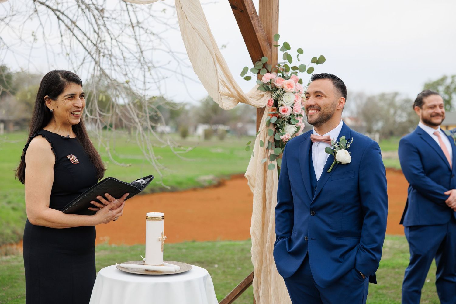 Wedding ceremony participants share joyful moments under an outdoor canopy during a countryside celebration.