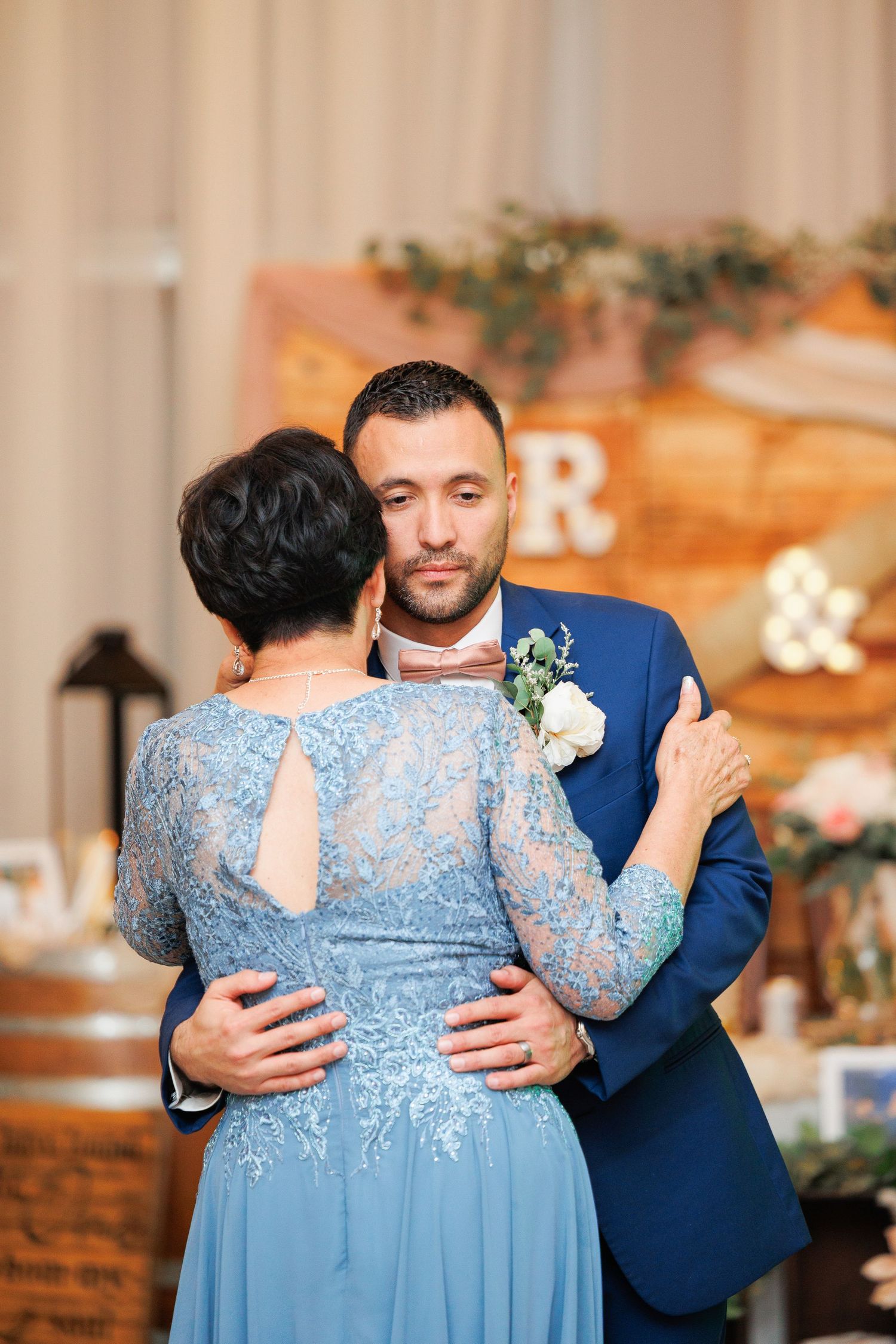 A couple shares an intimate moment at a wedding reception, with rustic wooden decor and floral arrangements in the background.