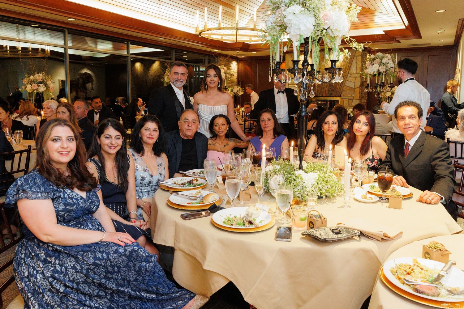 A large group of guests seated around an elegant dining table at a formal event with floral centerpieces and place settings.