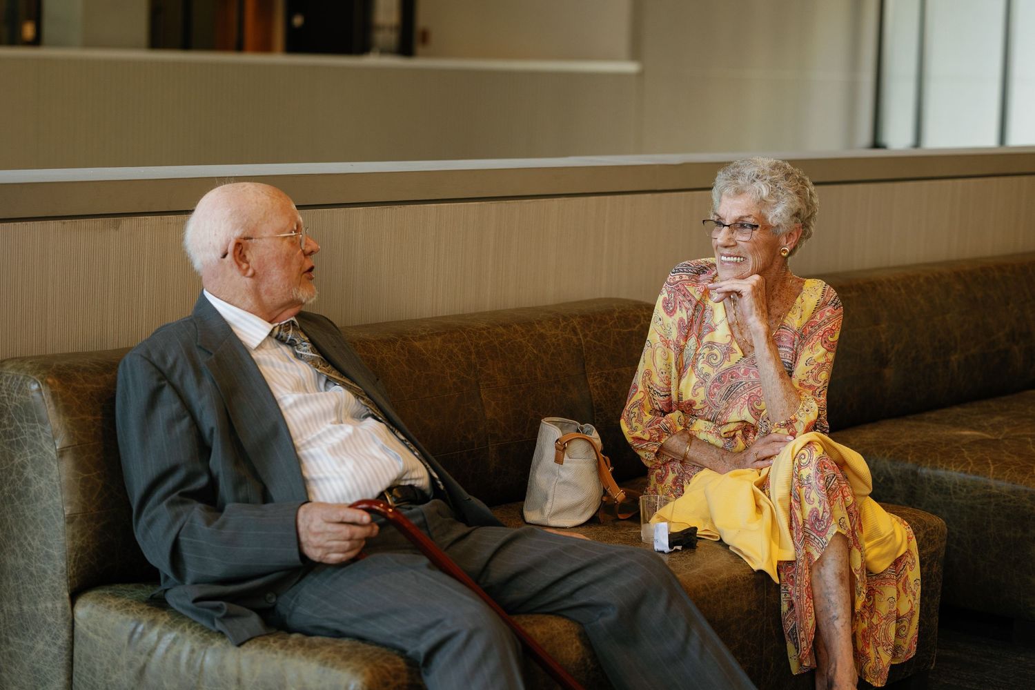 Elderly couple enjoying tea and conversation together in a casual indoor setting.