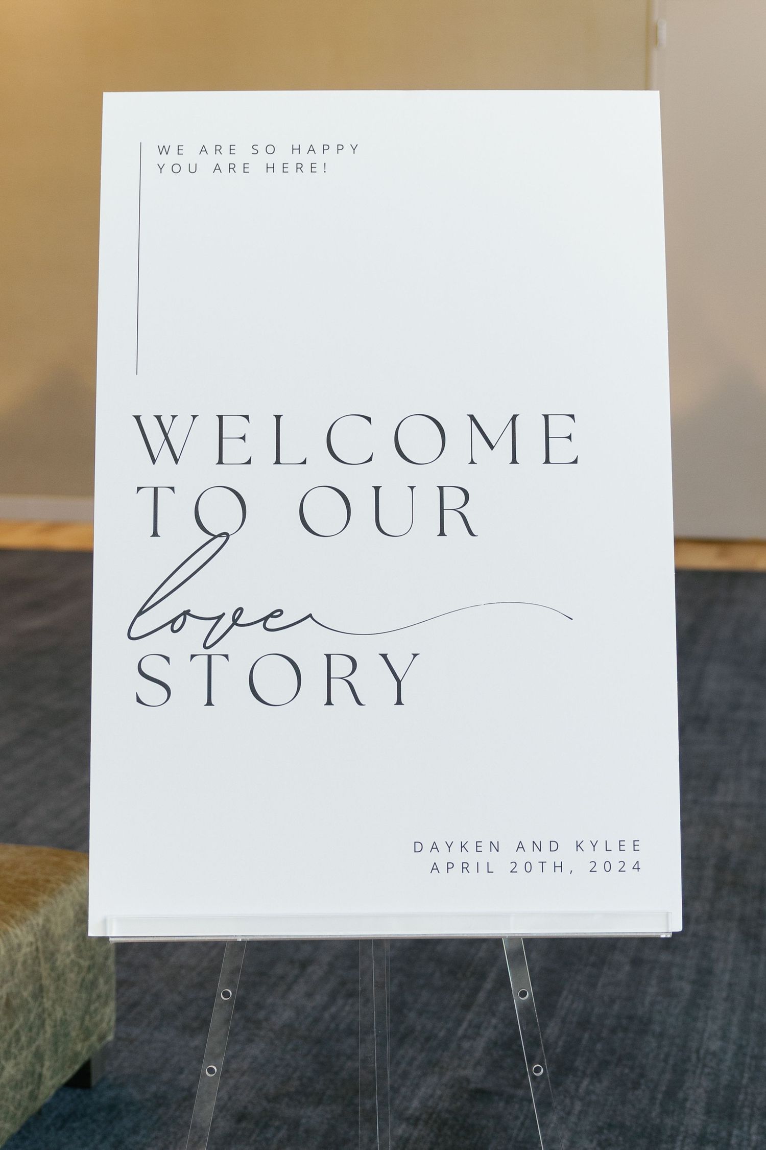 Elegant white wedding welcome sign with minimalist typography displaying 'Welcome to our story' on a dark textured surface.
