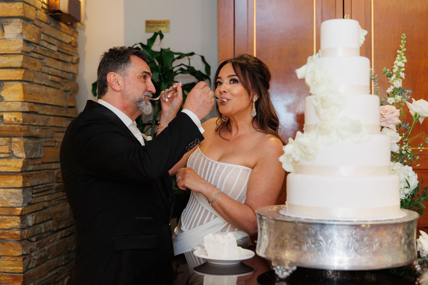 Wedding couple sharing a romantic moment next to an elegant white tiered cake at their reception.