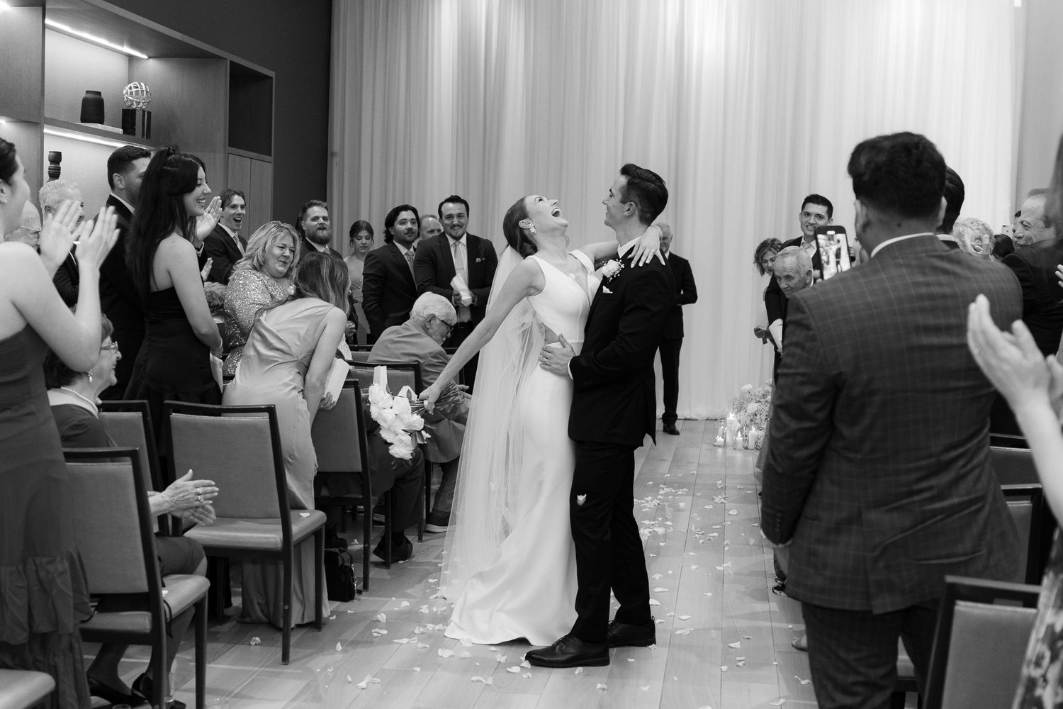 A couple shares their first dance at a wedding ceremony while guests watch and photographers capture the moment.
