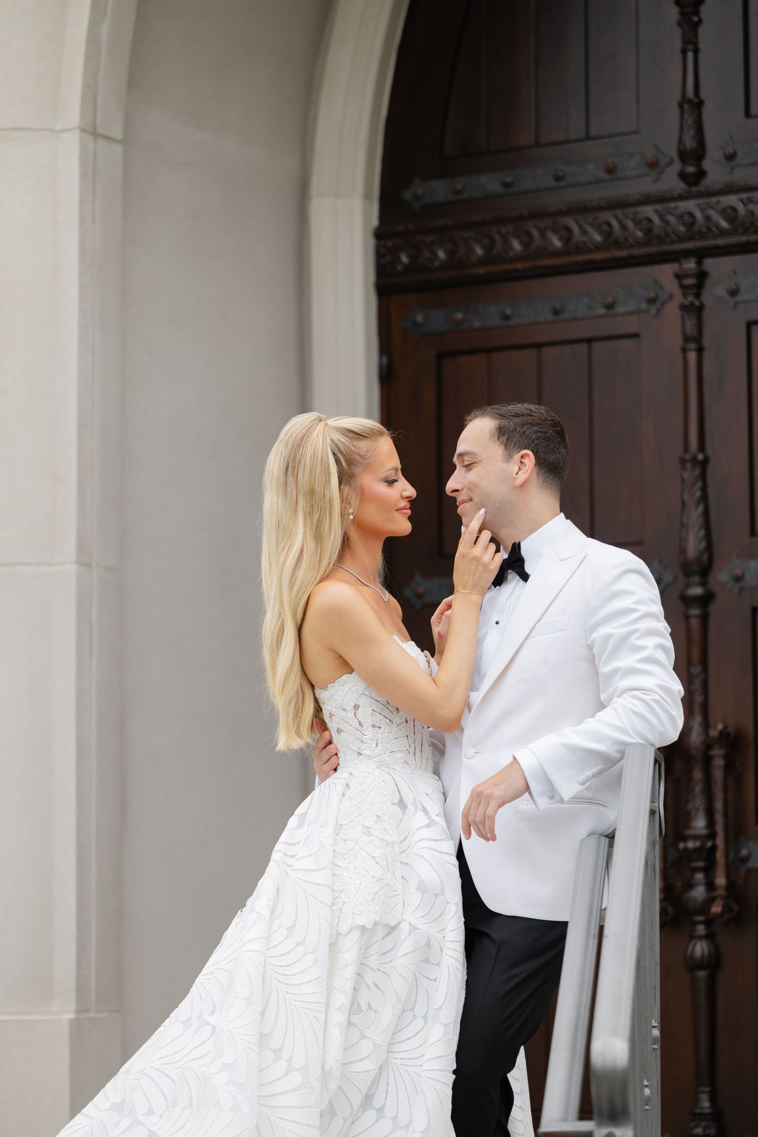 A romantic wedding couple shares an intimate moment on the steps of a grand building with white columns.